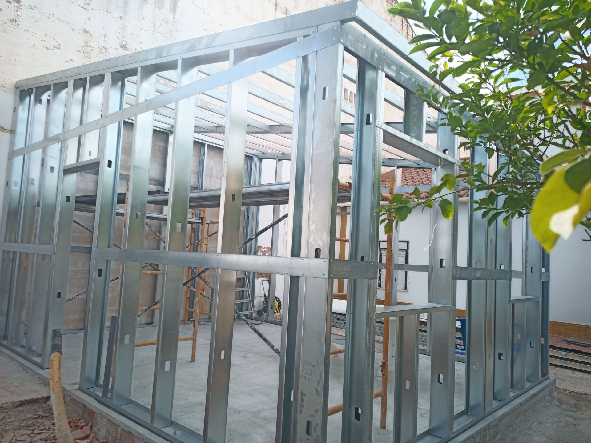 Construção com estrutura metálica de um pequeno edifício, ao ar livre. Estrutura das paredes e do telhado visíveis.