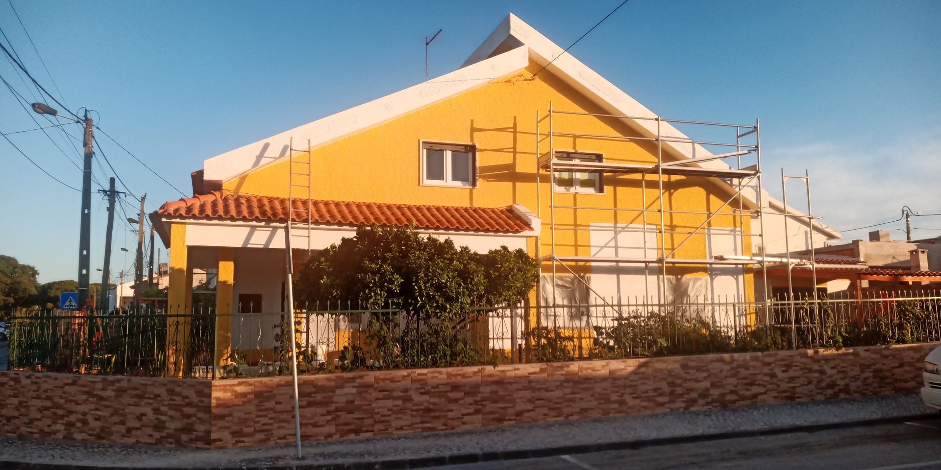 Casa amarela em reforma com andaimes. Telhado de telha vermelha e céu azul.