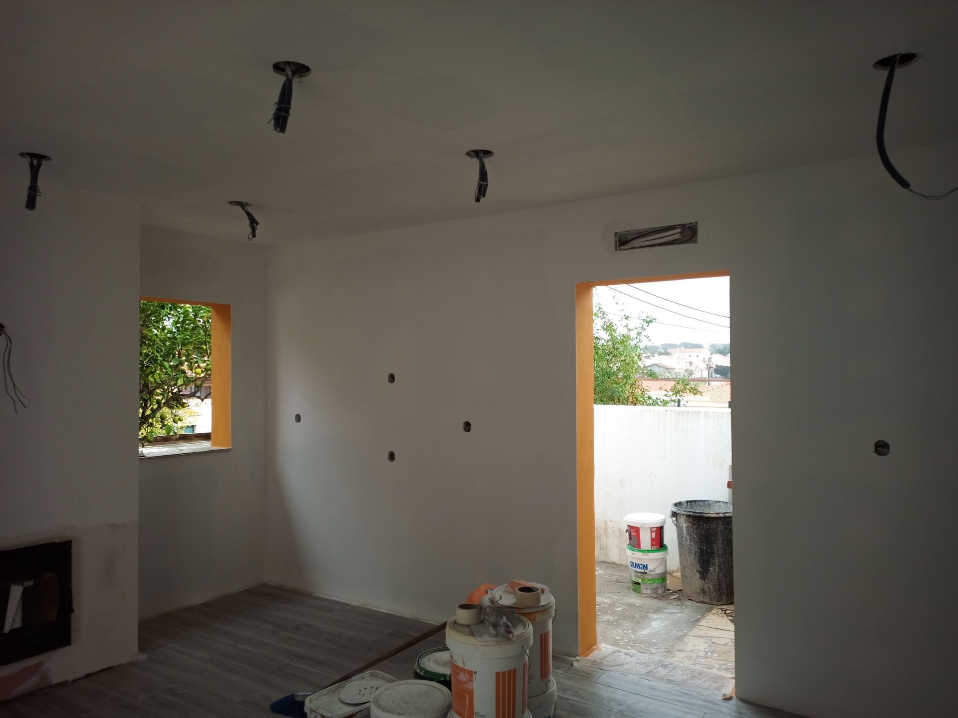 Sala interna em construção, com paredes brancas, fiação exposta e porta.