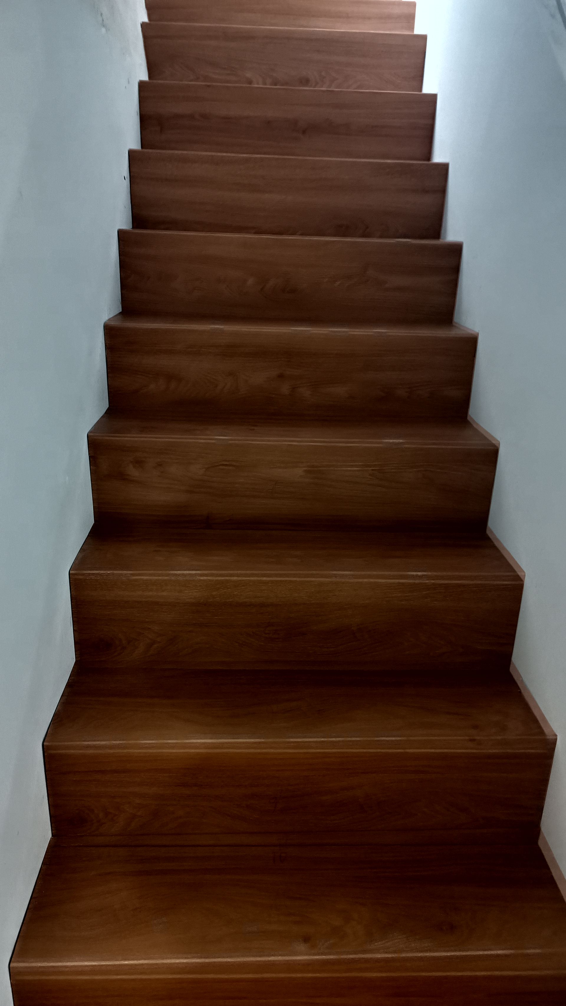 Escada de madeira ascendente, emoldurada por paredes brancas.