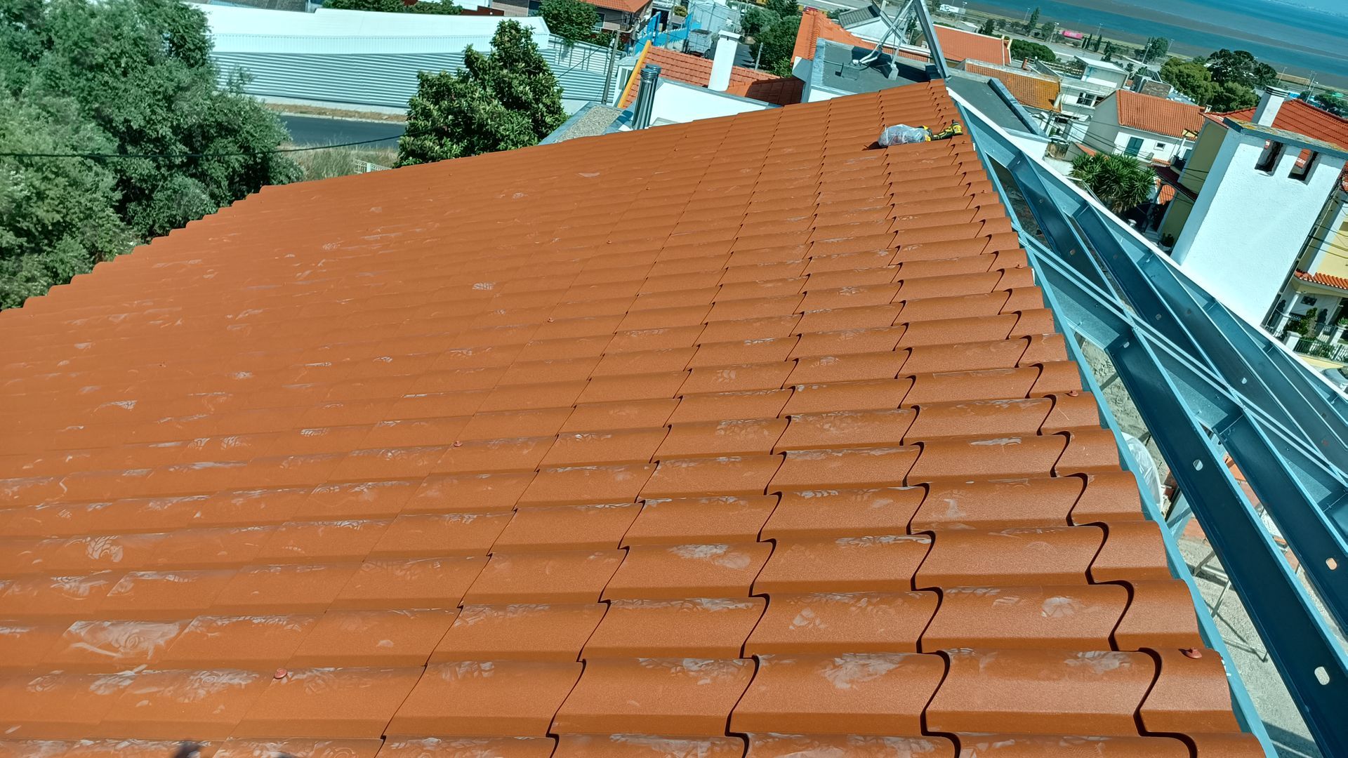 Telhado de telha vermelha com painéis solares, com vista para a cidade em um dia ensolarado.