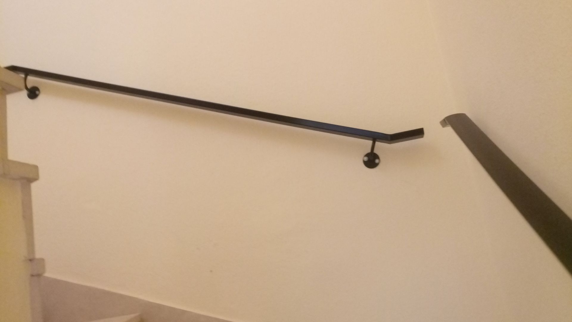 Corrimão de metal preto em parede branca, ao longo da escada.