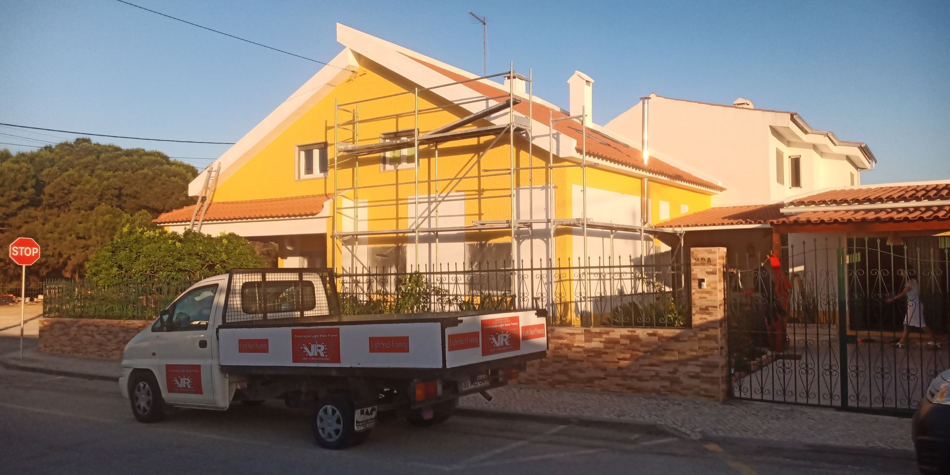 Uma casa amarela com andaimes e uma caminhonete branca estacionada em frente.