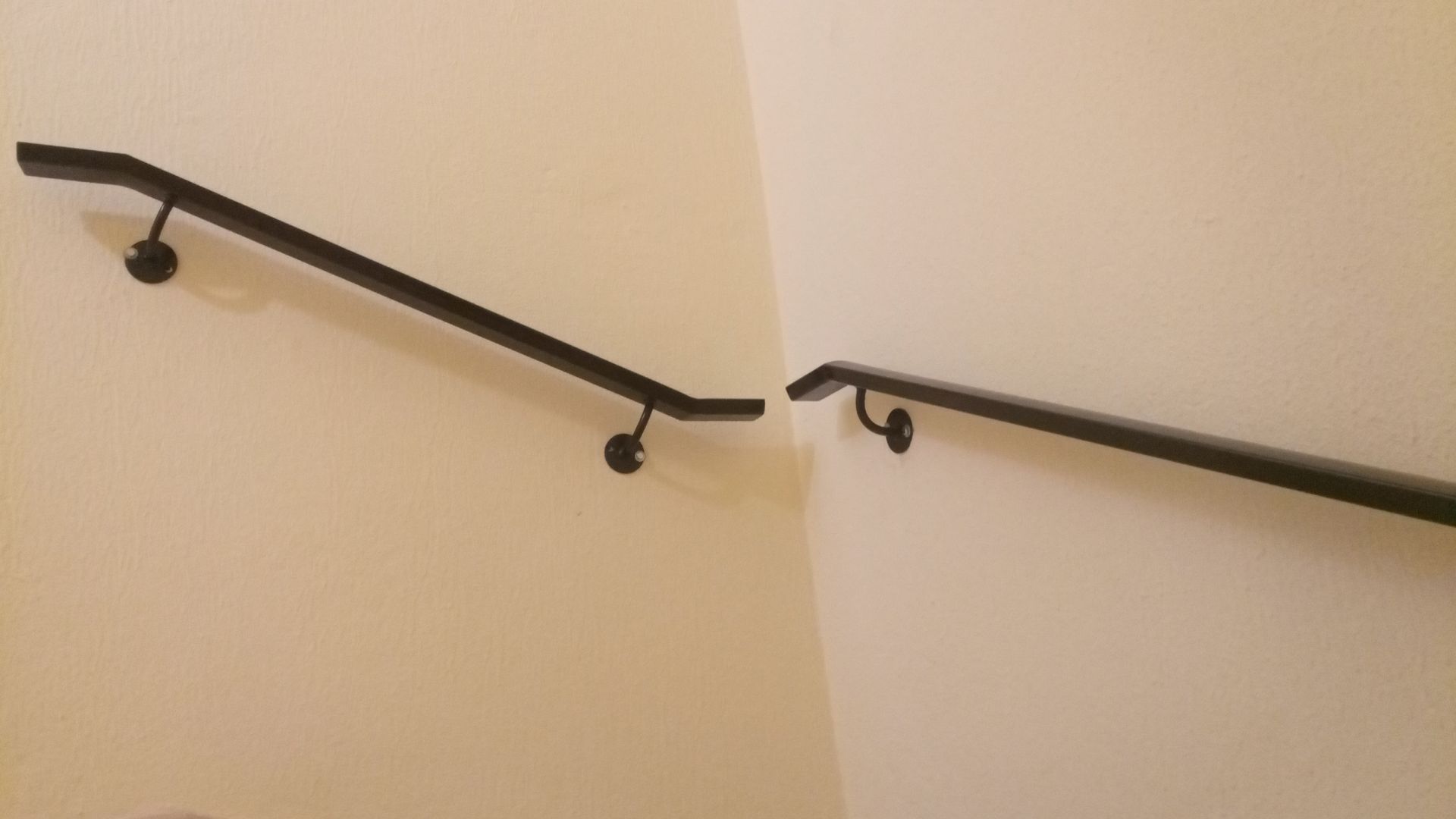 Corrimãos pretos fixados em paredes esbranquiçadas, formando um canto.