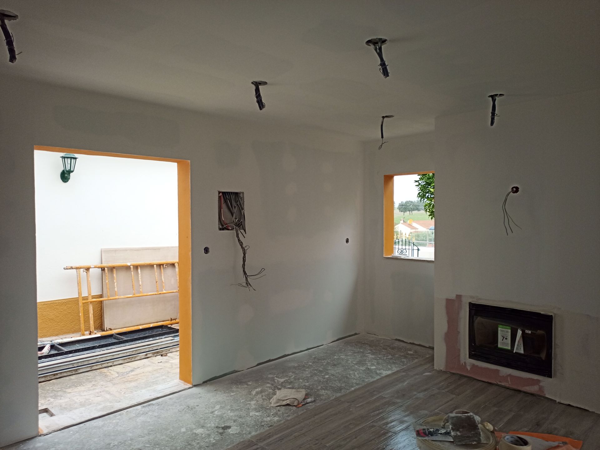 Quarto interior em construção com fiação exposta, porta aberta, janela e lareira.