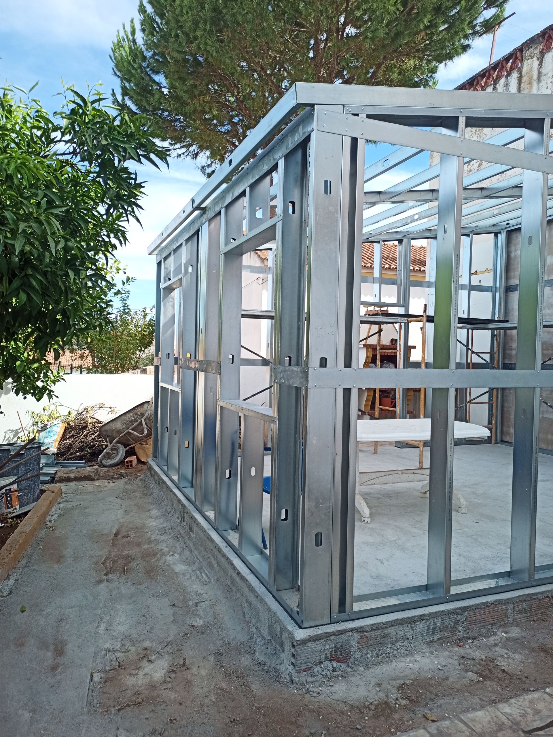 Estrutura metálica de um edifício em construção, vista exterior, com aberturas de janelas e portas visíveis.