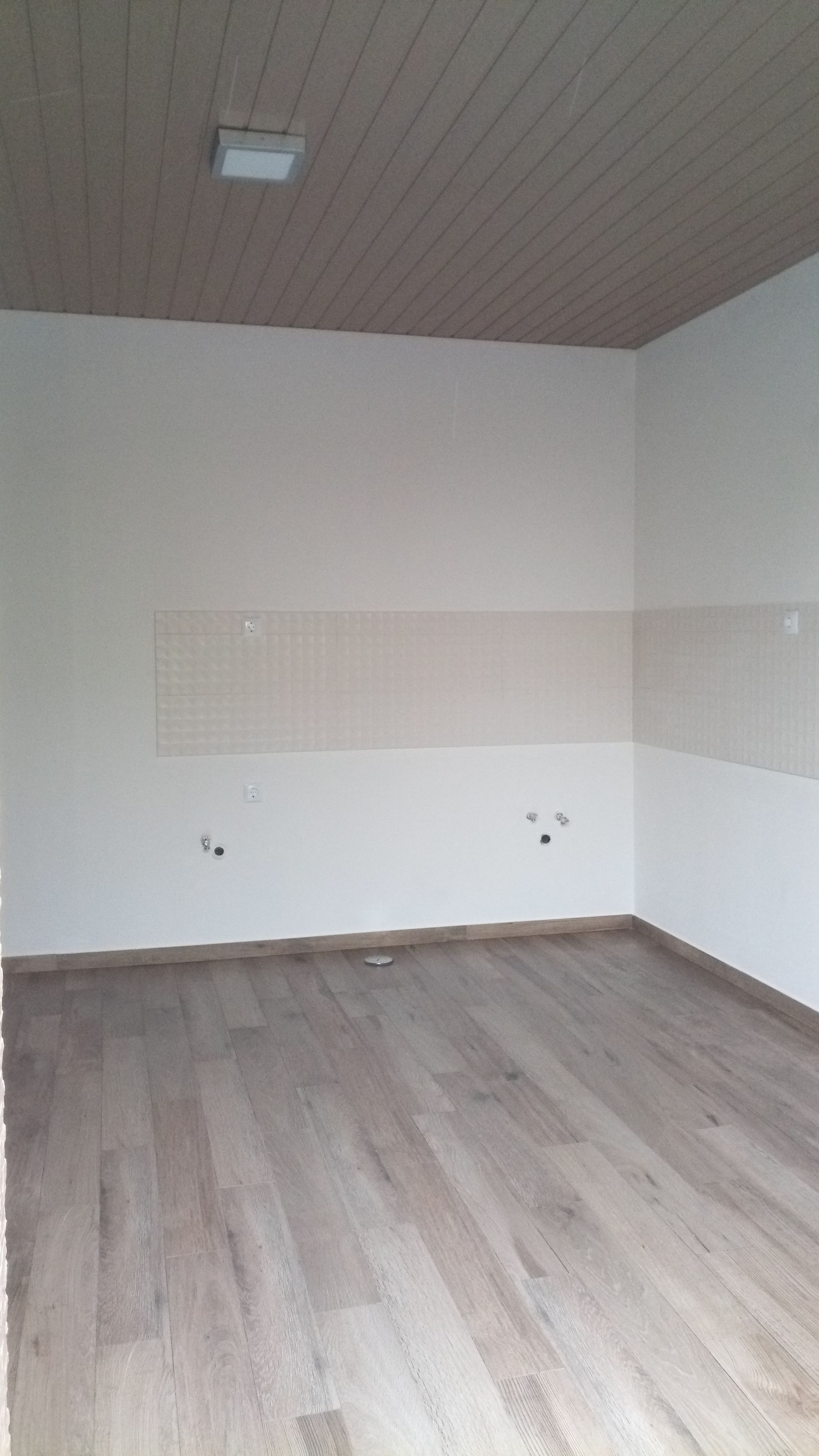 Quarto vazio com piso de madeira clara, paredes brancas e teto com painéis de madeira.