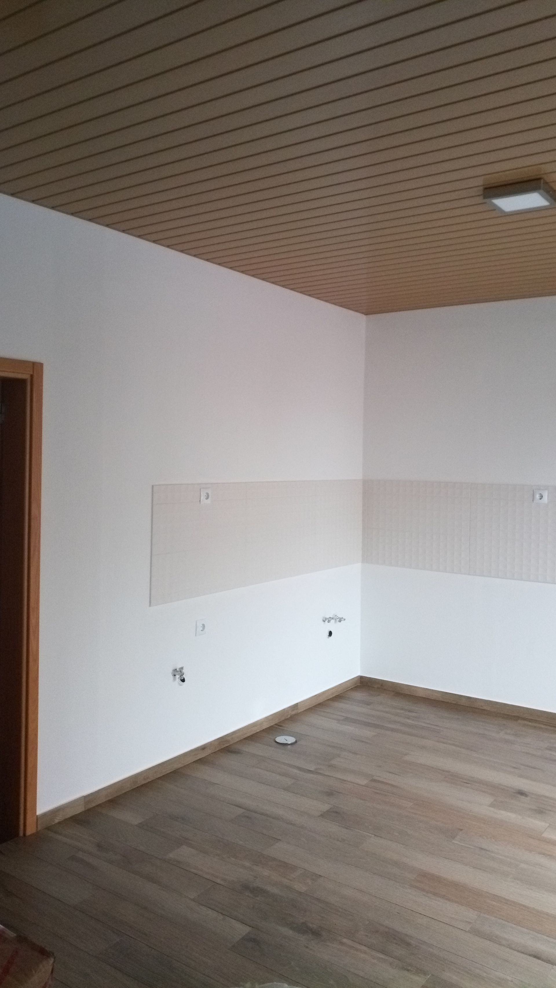 Sala vazia com piso de madeira, paredes brancas e teto com painéis de madeira.