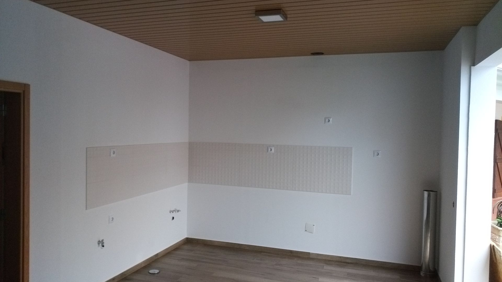 Sala vazia com paredes brancas, teto de madeira e piso de azulejo. Um rolo de tecido está em um canto.