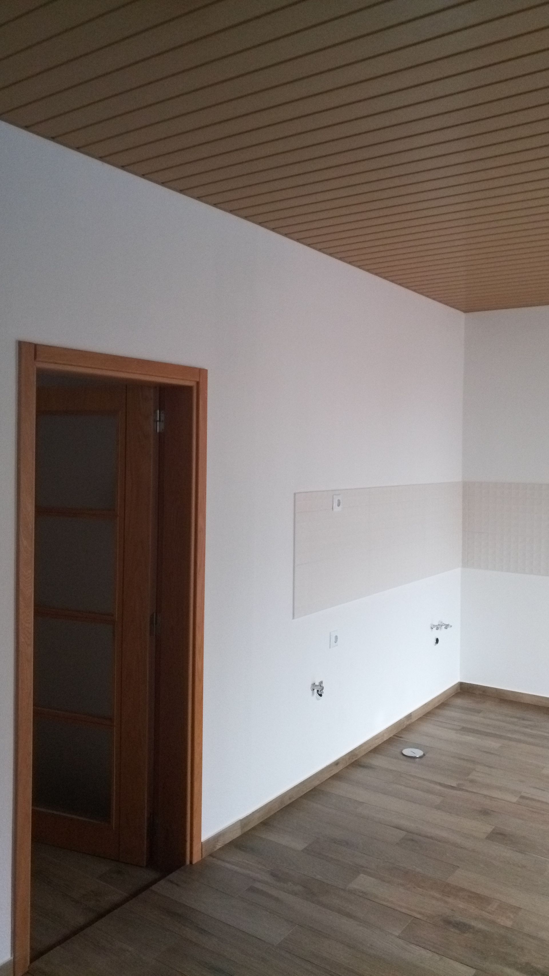 Quarto interior com teto, batente da porta e piso de madeira, paredes brancas.