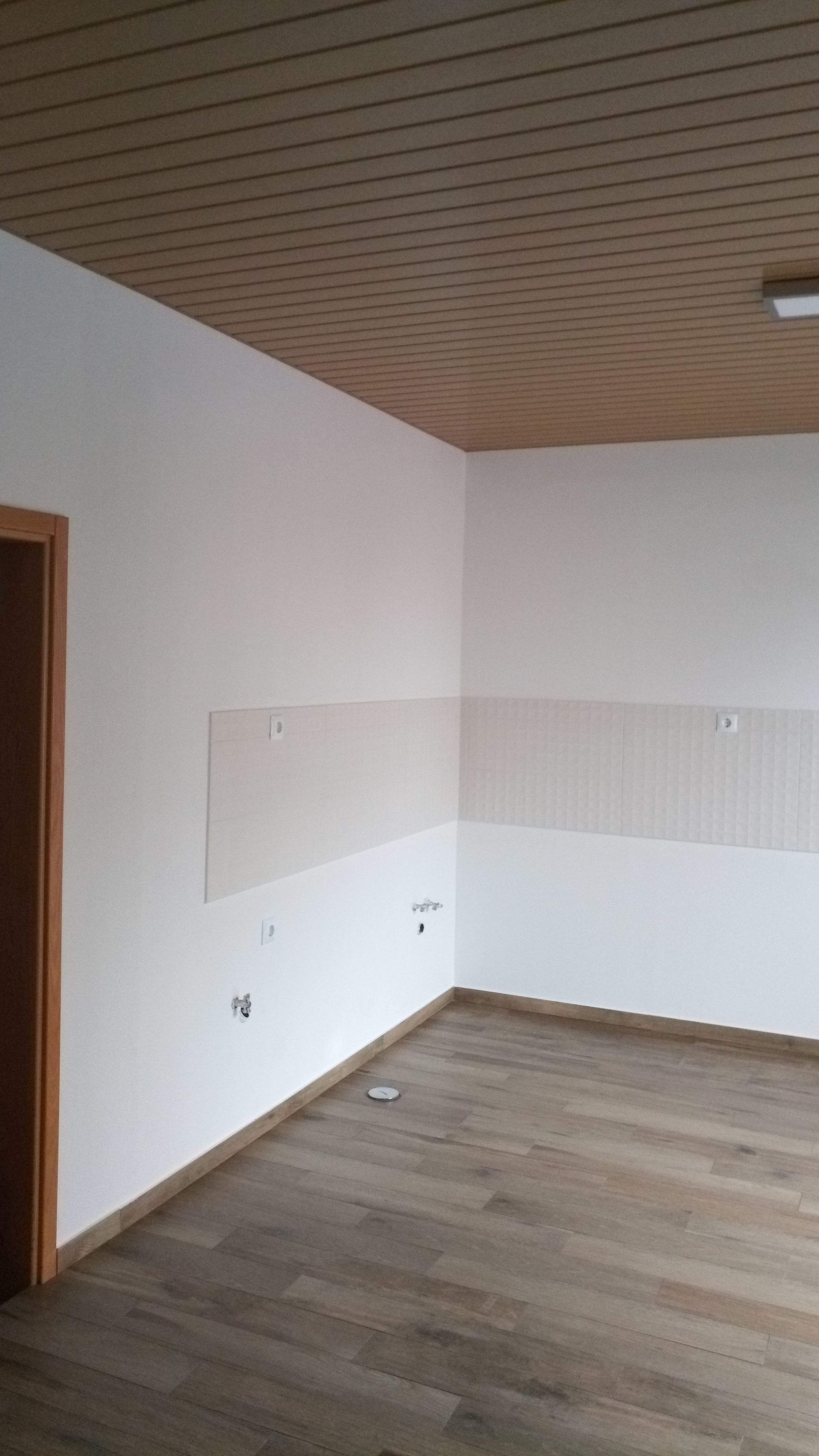 Quarto vazio com teto de madeira, paredes brancas e piso de madeira.