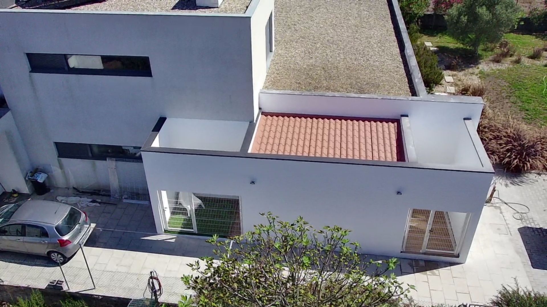 Casa moderna branca com telhado de telhas vermelhas, carro estacionado na entrada da garagem, pessoa caminhando.