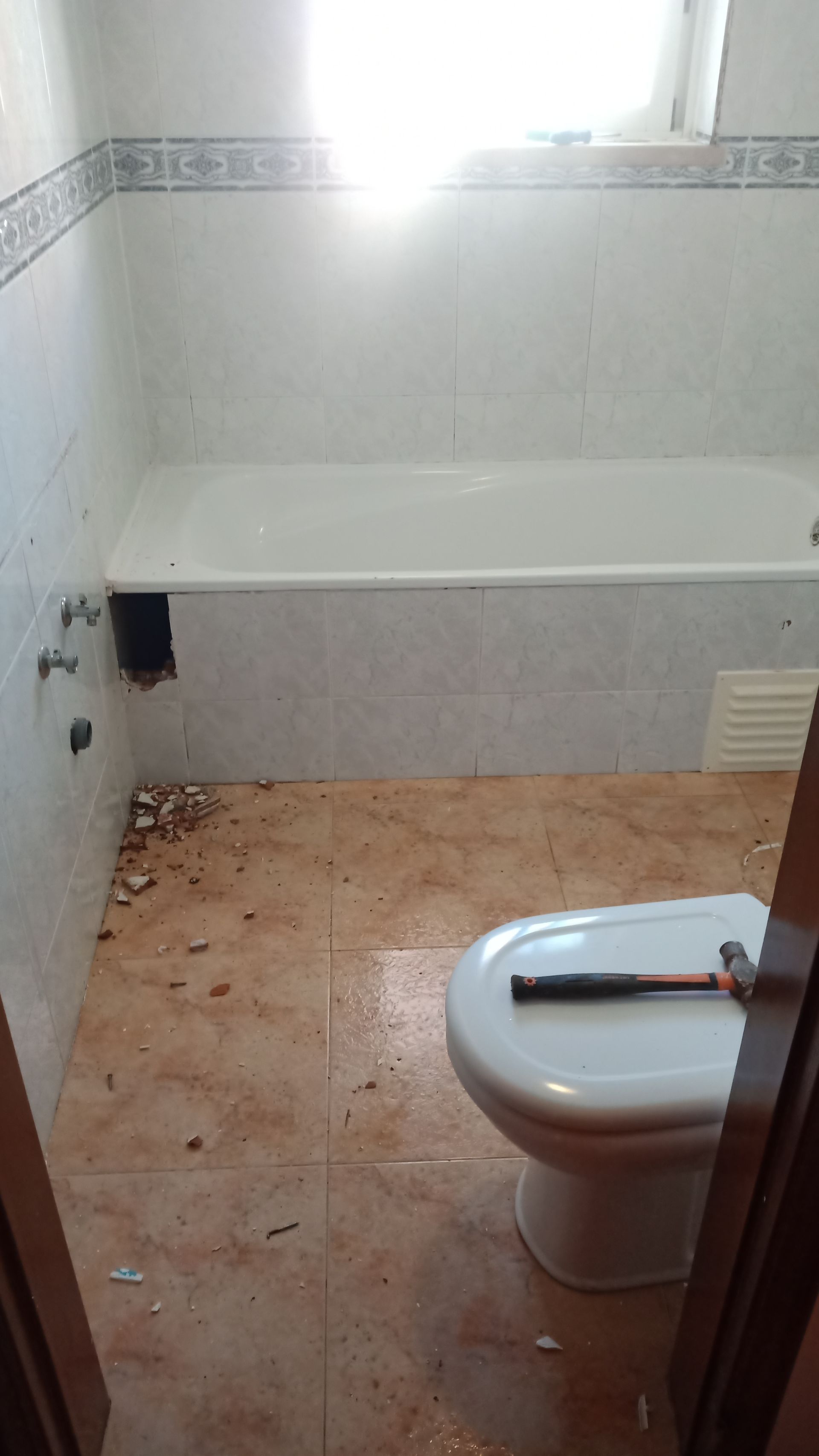 Banheiro em reforma, com banheira, vaso sanitário e entulho no piso de azulejo.