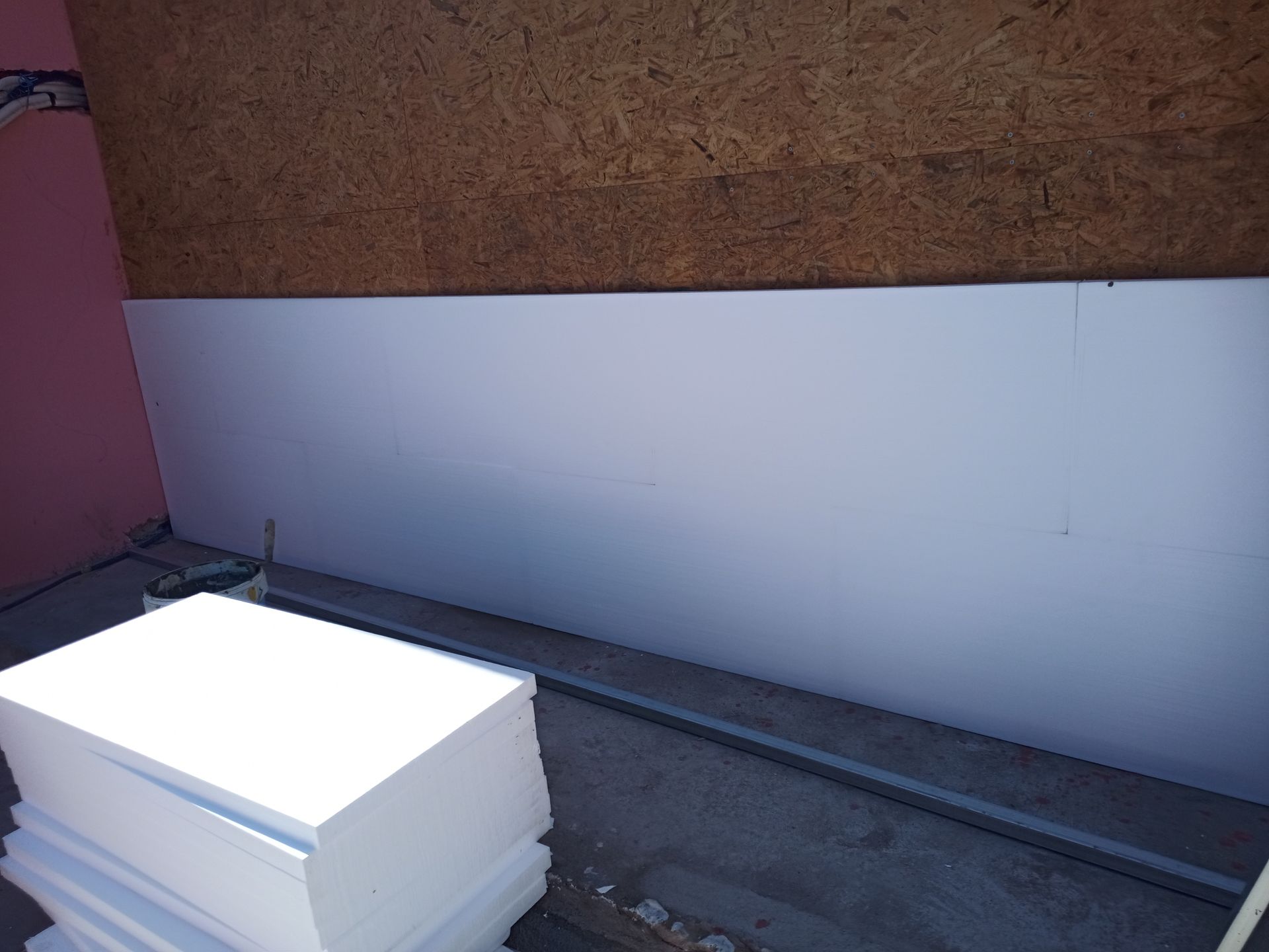 Painéis isolantes brancos contra uma parede marrom; blocos de espuma branca empilhados em primeiro plano.