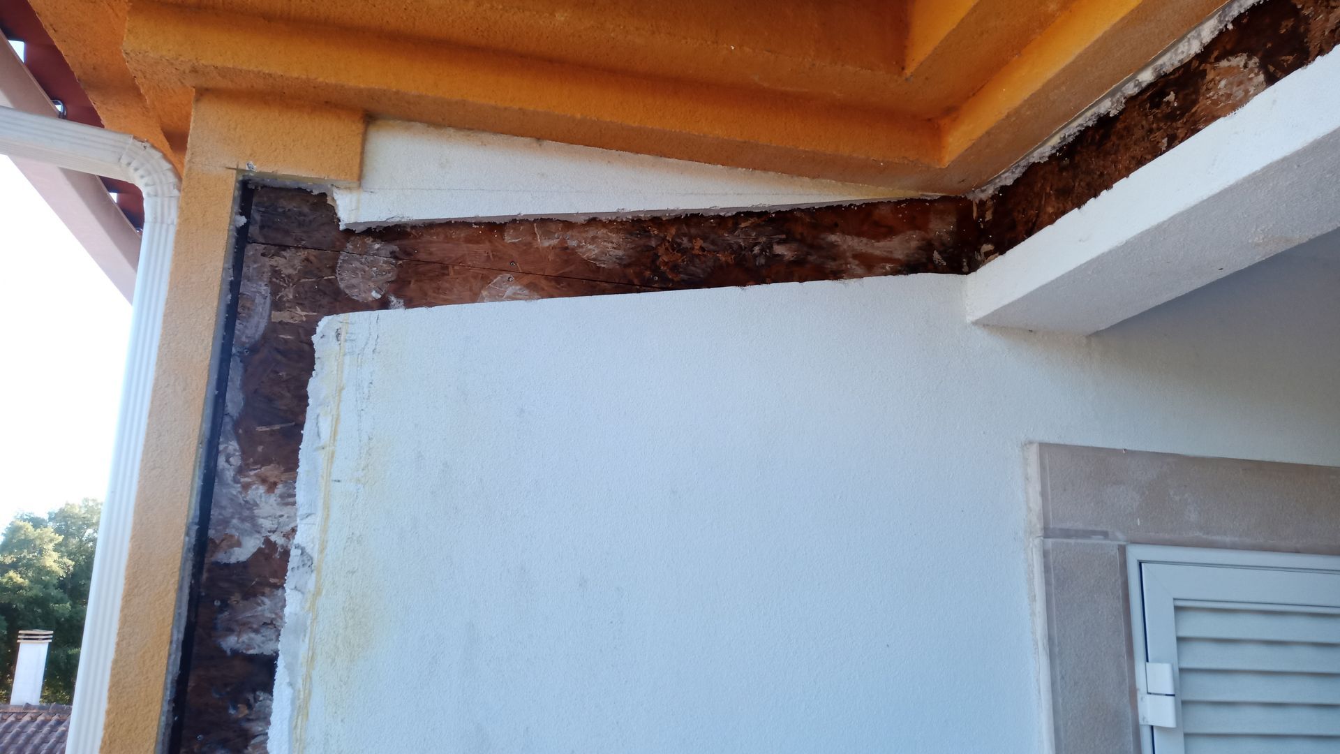 Canto exterior de um edifício com reboco danificado, expondo tijolos e vigas de madeira.