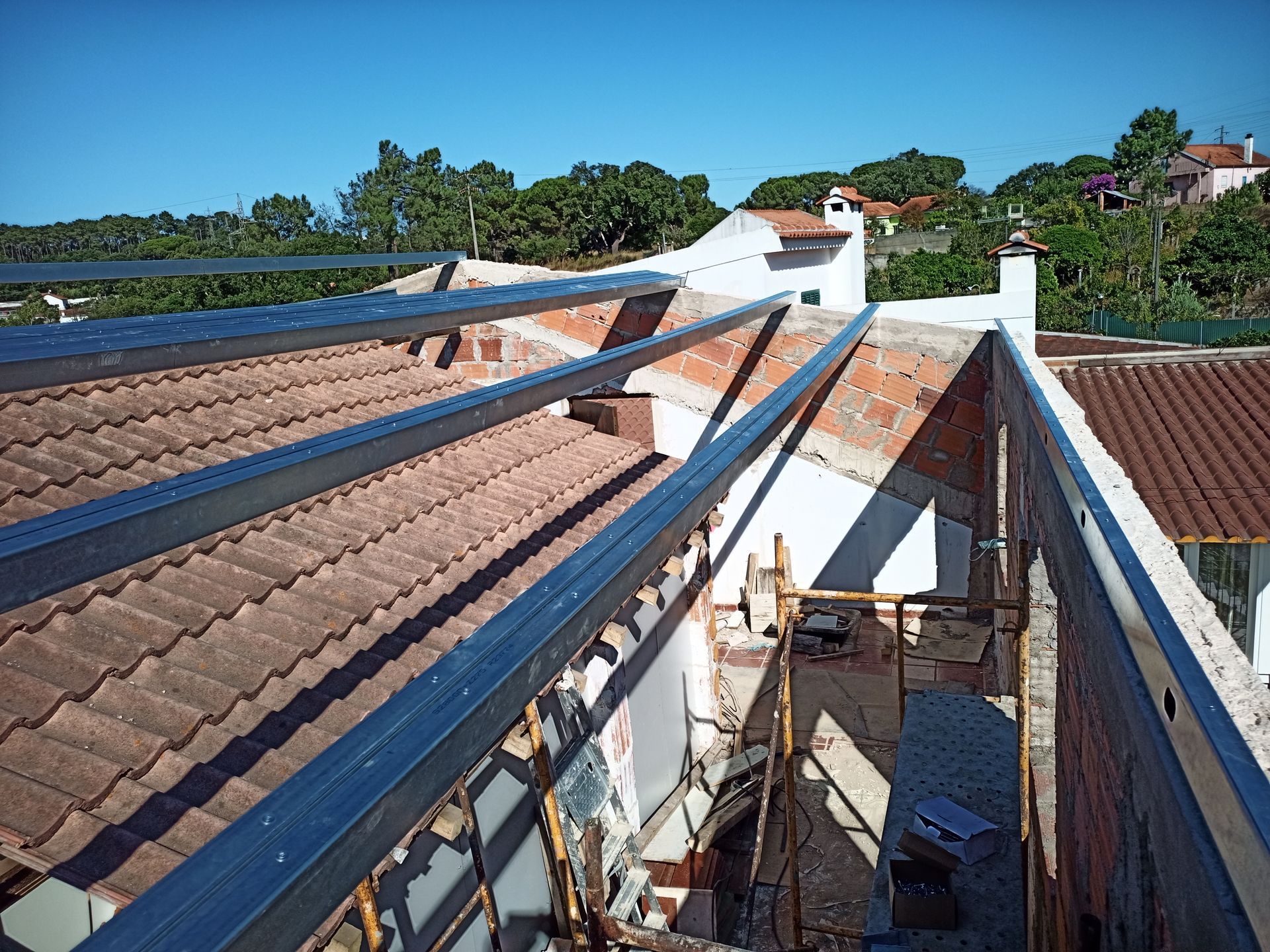 Telhado em construção com vigas metálicas sobre telhas. Obra em andamento em um dia ensolarado.