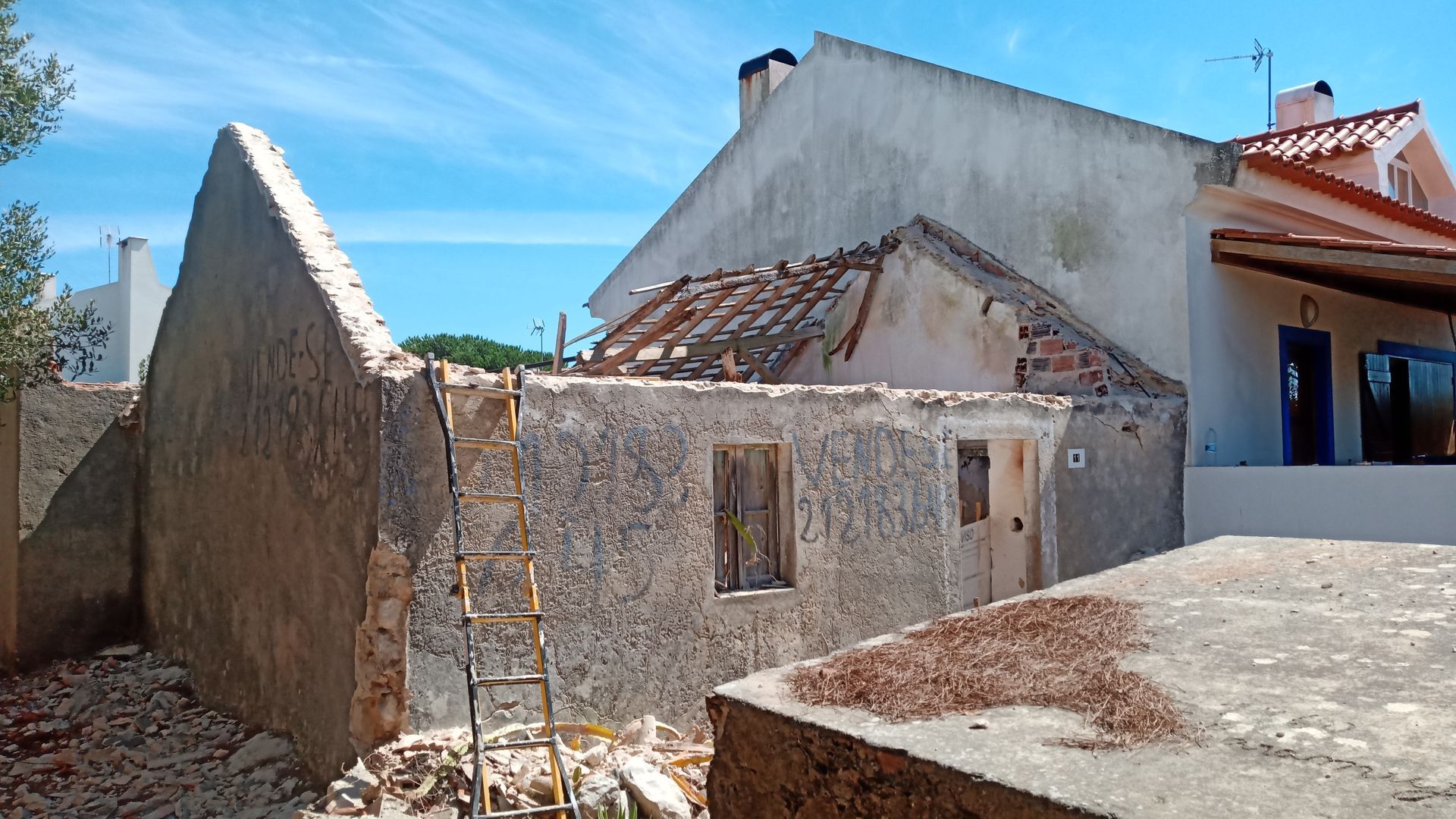 Edifício de pedra parcialmente demolido com escada, adjacente a outras estruturas.