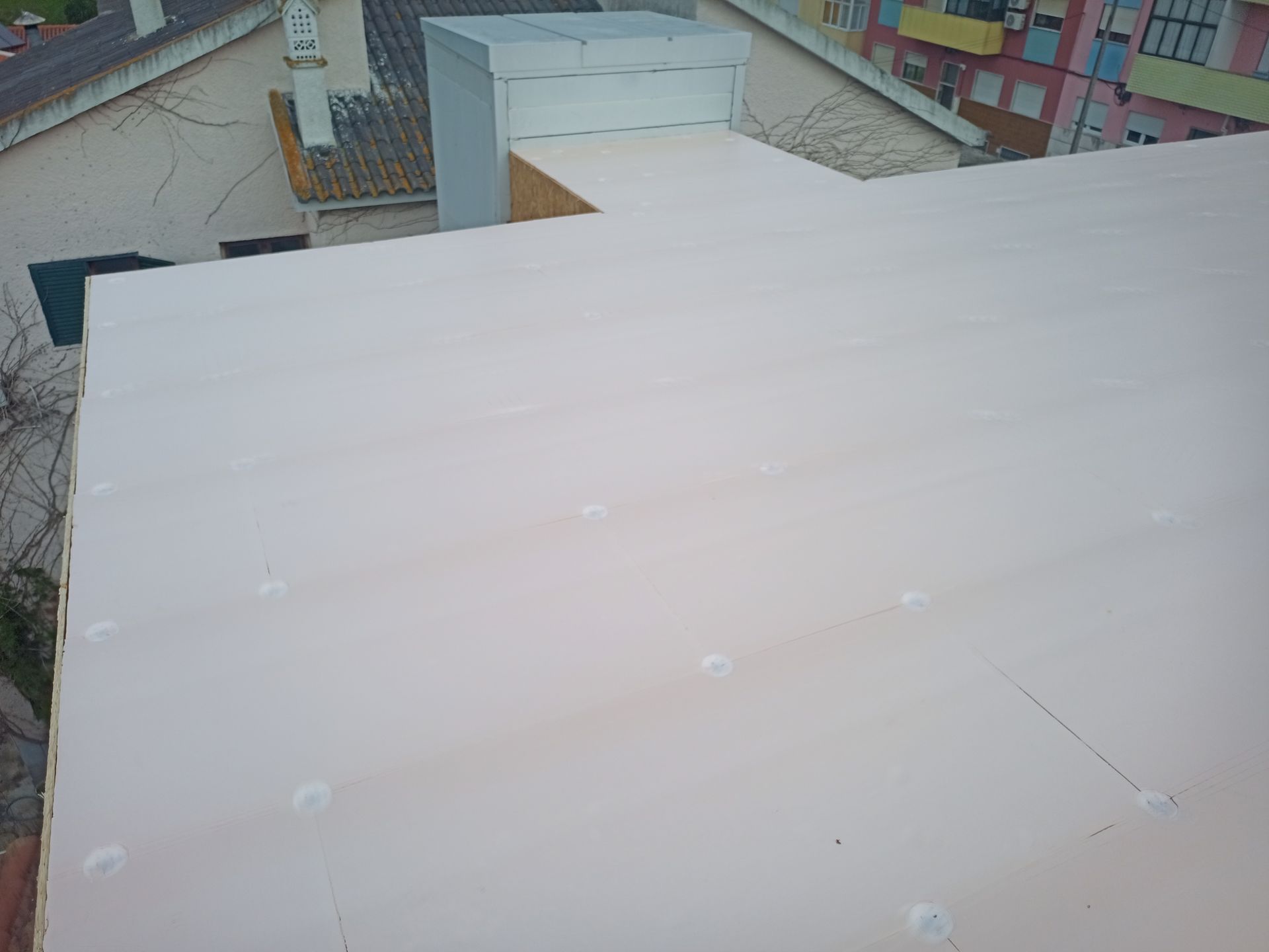 Vista de um telhado plano de cor clara com saliências brancas dispersas, com edifícios ao fundo.