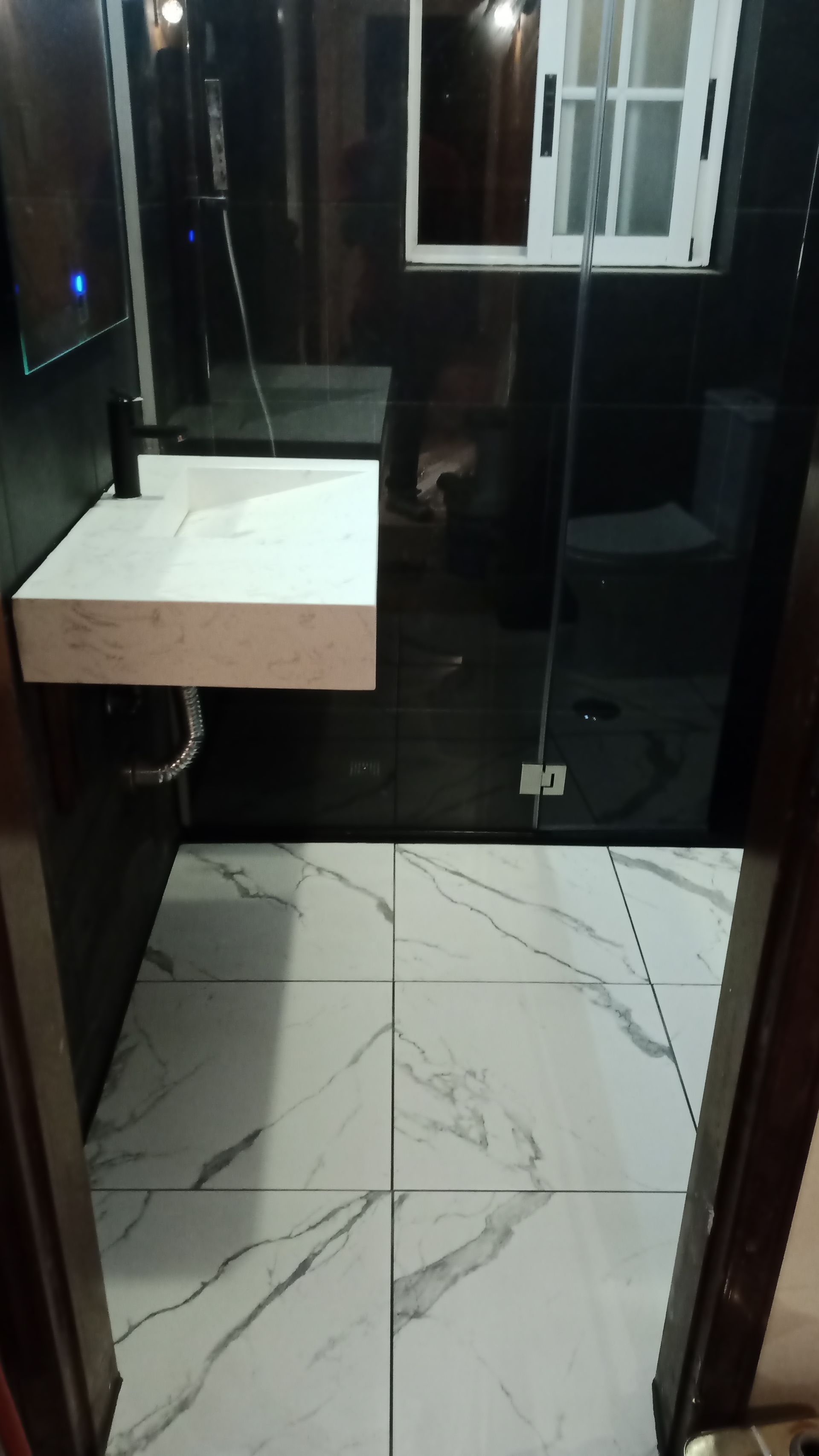 Banheiro moderno com piso e pia de mármore branco, paredes pretas e box de vidro.