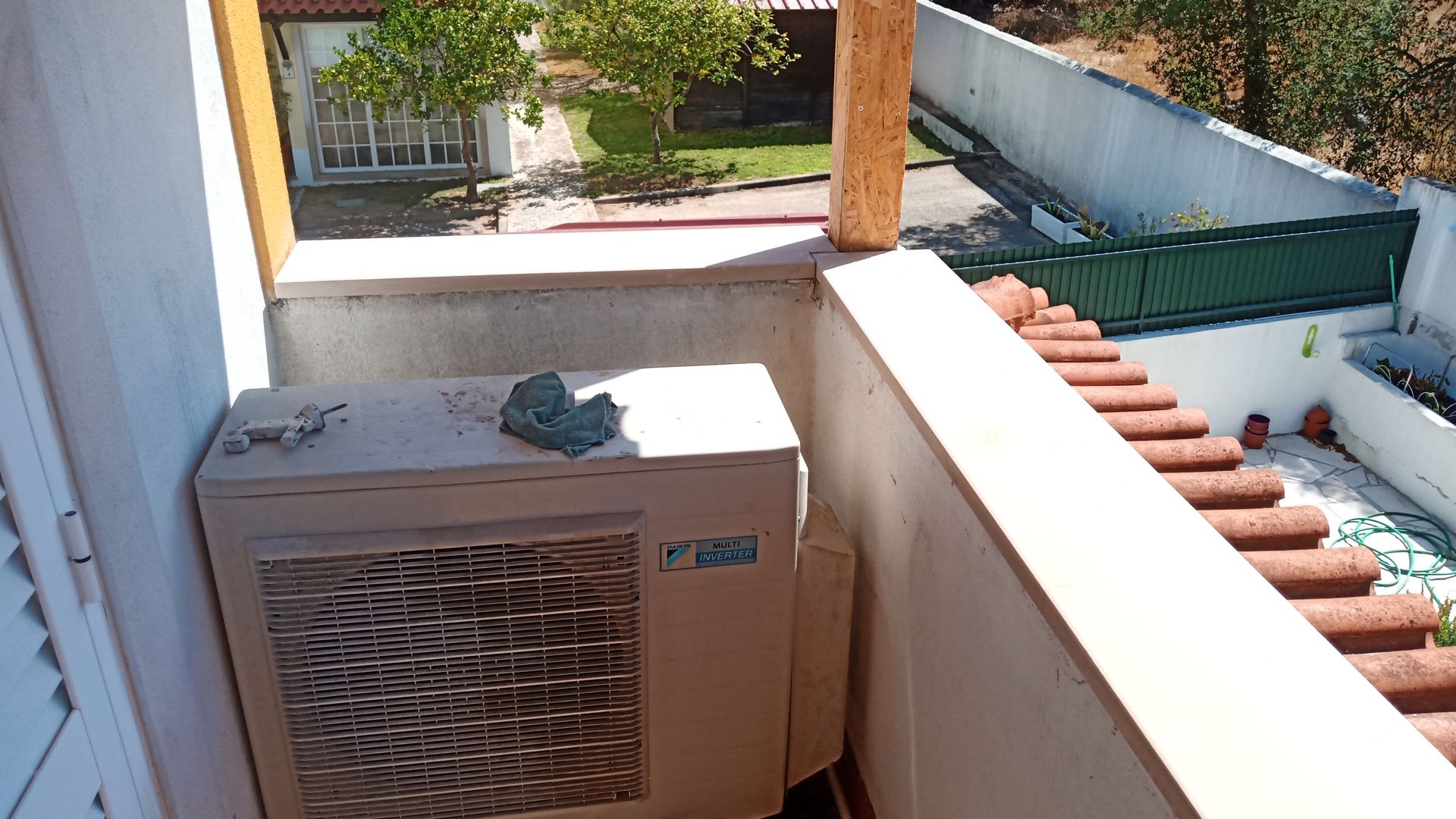 Aparelho de ar condicionado em uma varanda com vista para um jardim e outros edifícios.