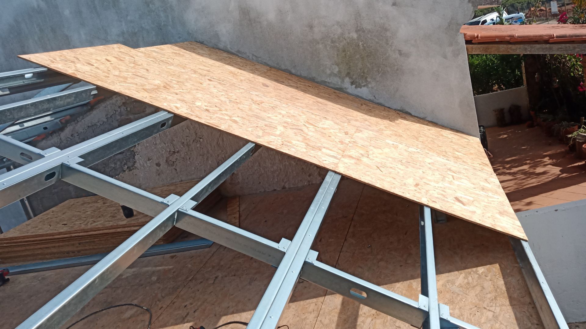 Placa OSB sendo colocada em uma estrutura de telhado com armação metálica próxima a uma parede.