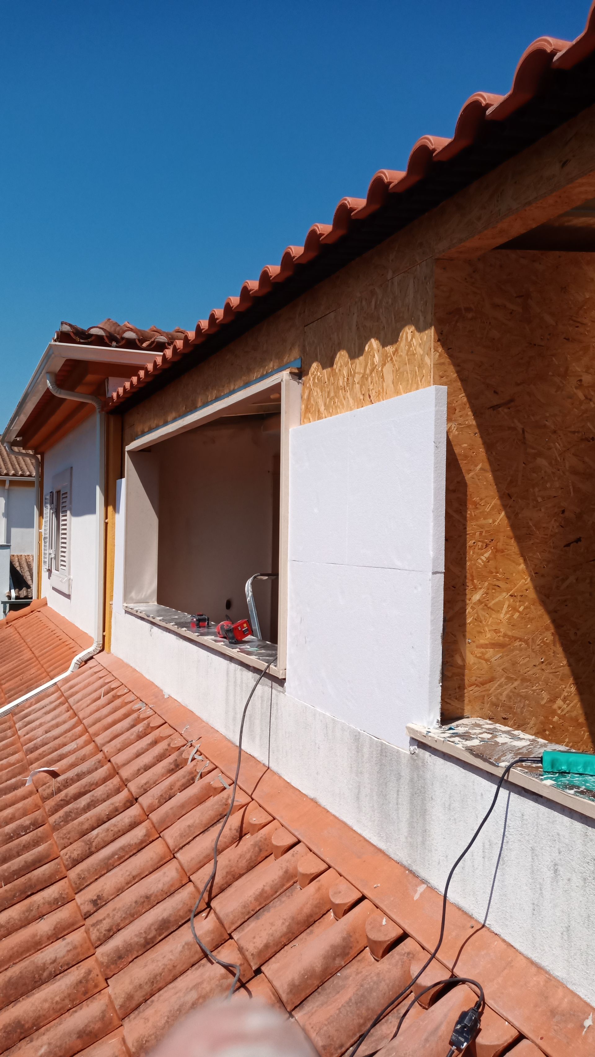 Canteiro de obras: trabalhos em caixilho de janela, vista parcial do telhado, céu azul.