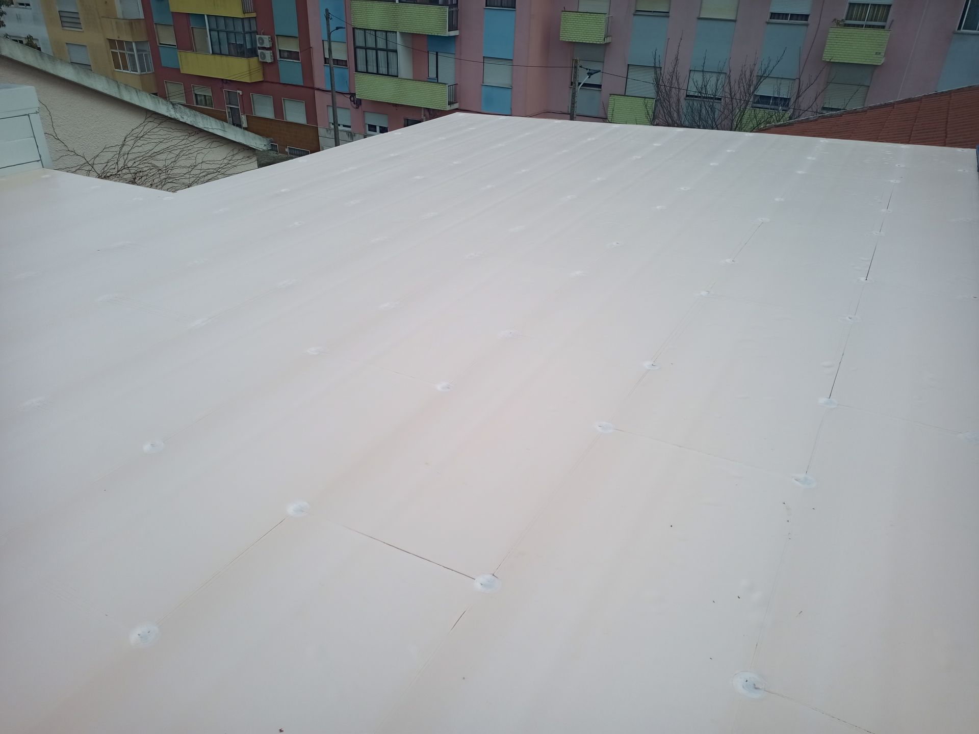 Telhado de metal ondulado branco com prédio ao fundo.