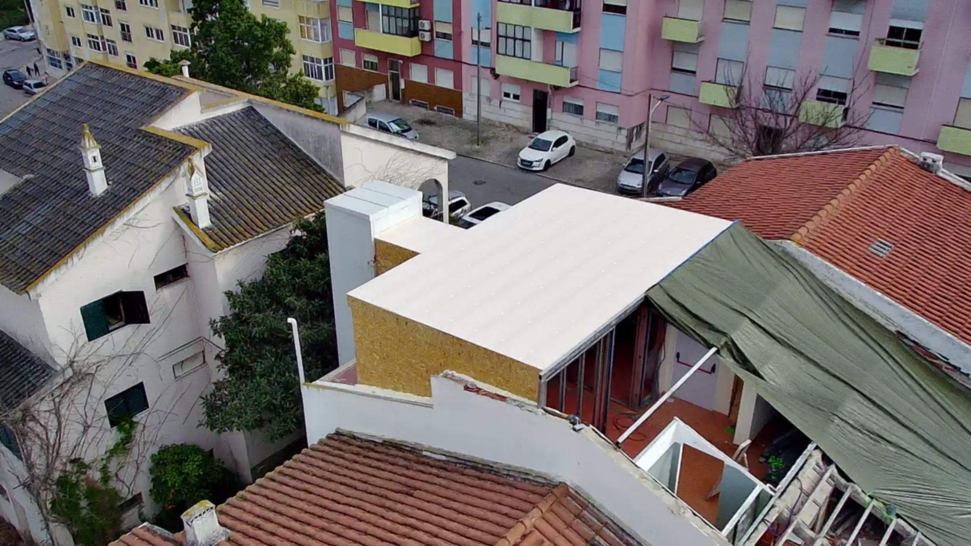 Vista aérea de edifícios urbanos com telhados e carros estacionados em uma rua.