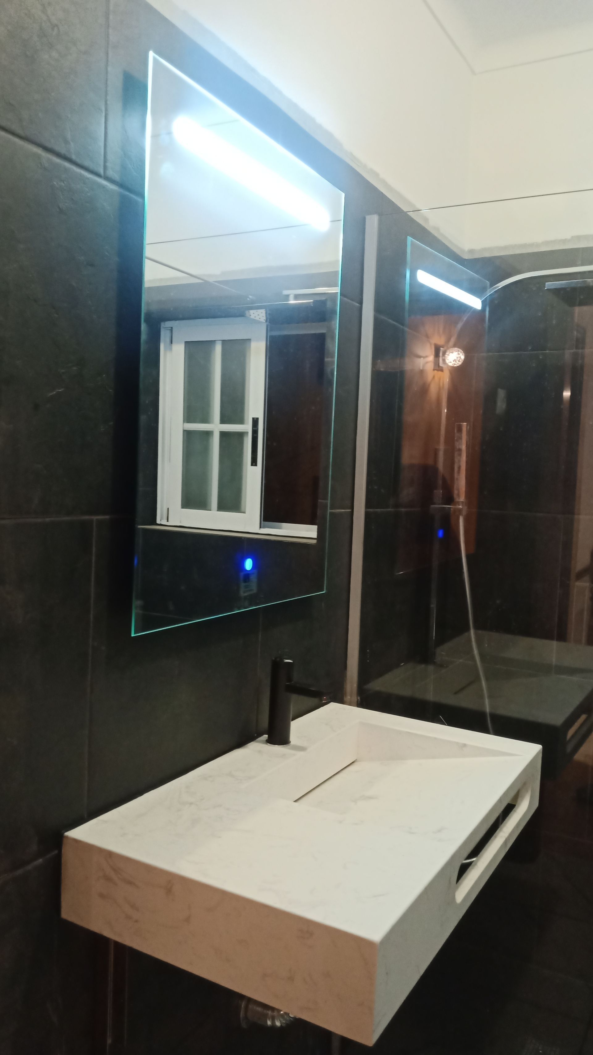 Banheiro moderno com pia branca, torneira preta e espelho retangular com moldura iluminada.