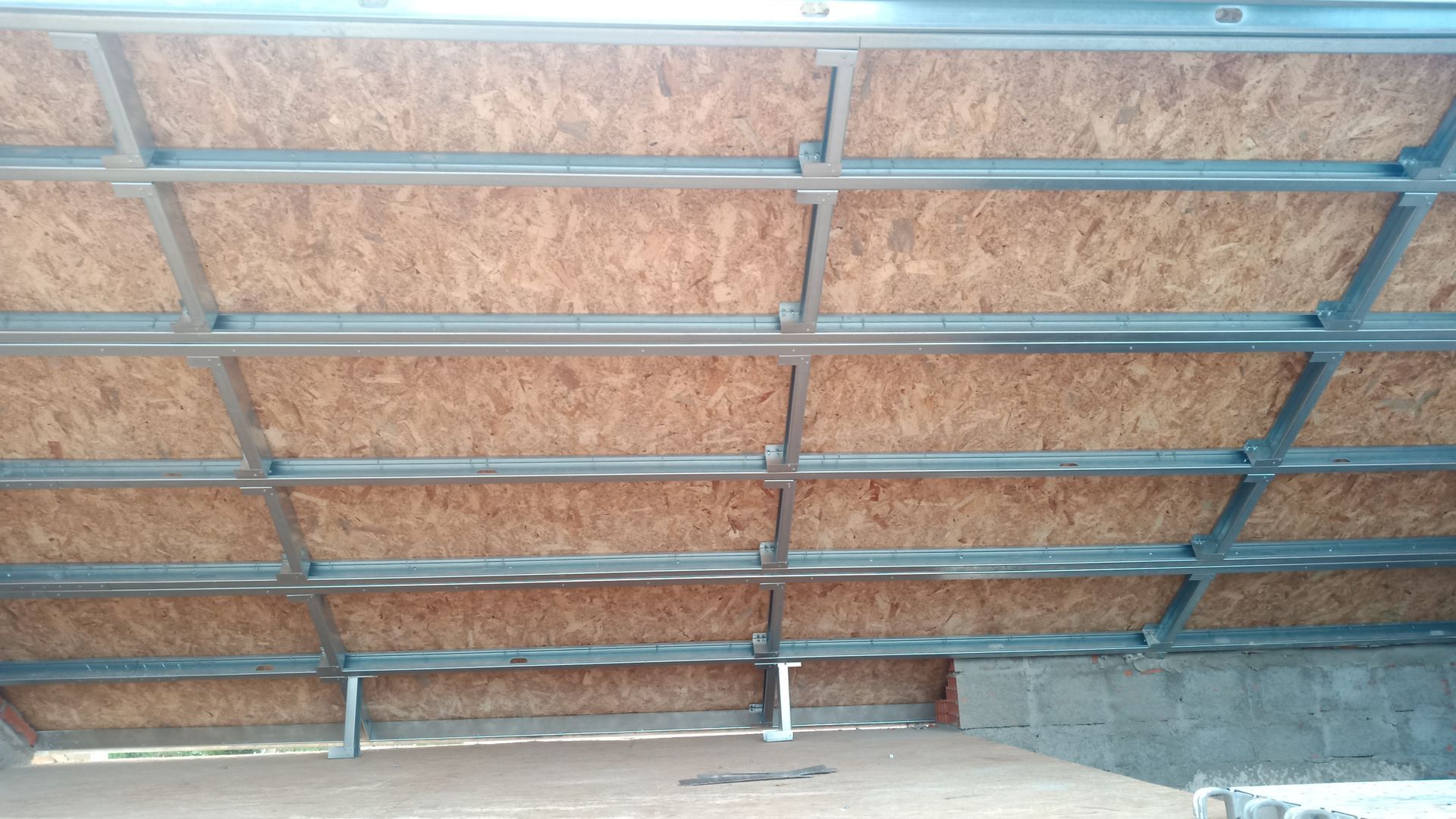 Placas de OSB marrom instaladas entre perfis metálicos, formando um teto.