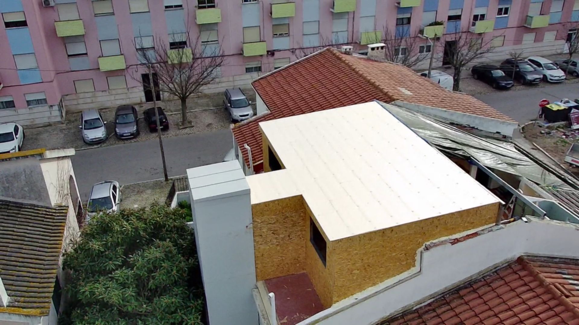 Vista aérea de prédios e carros estacionados. Um dos prédios tem um telhado claro com aparência nova.