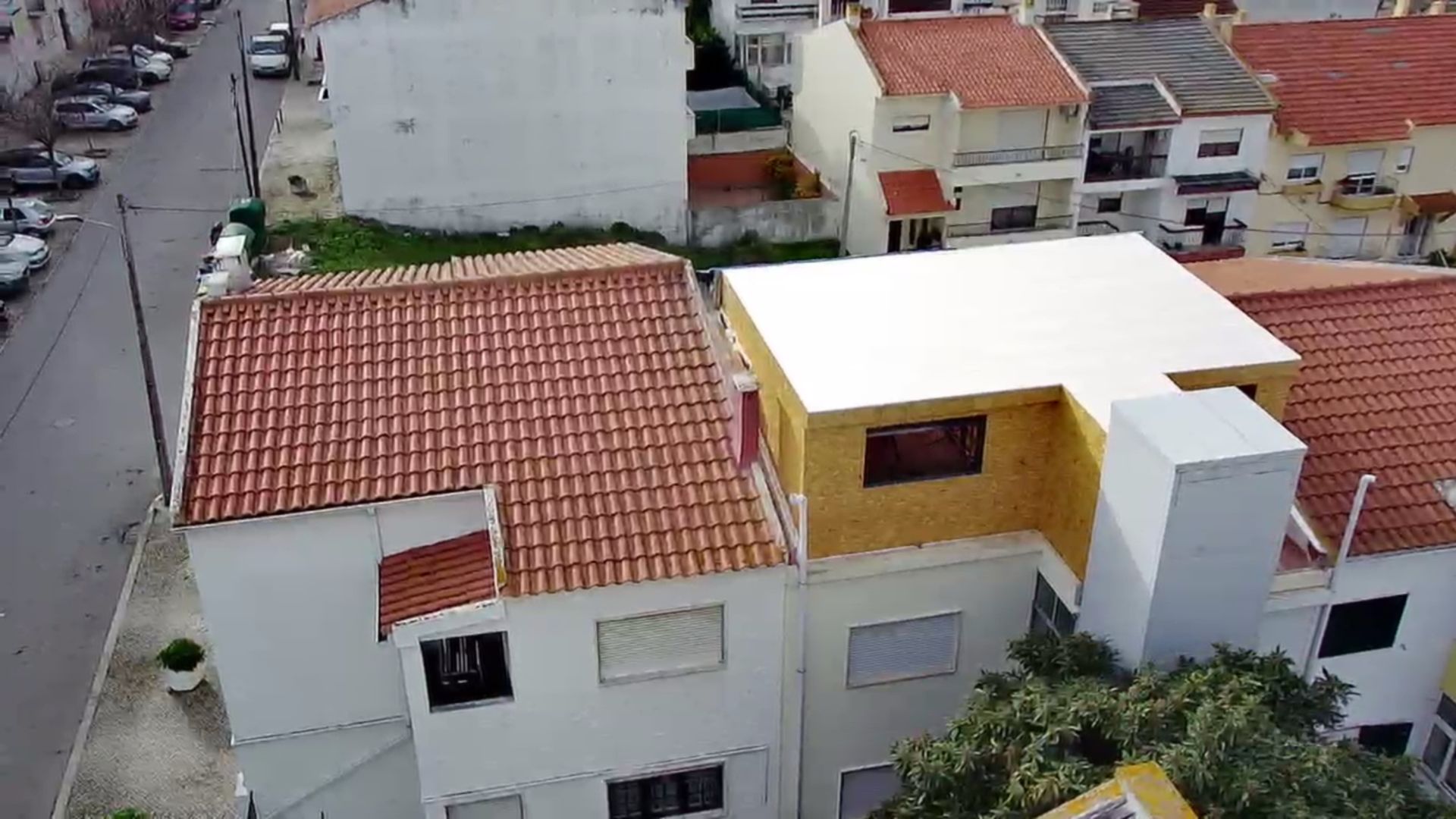 Vista aérea de edifícios residenciais com telhados de telha vermelha e um edifício com telhado plano branco.
