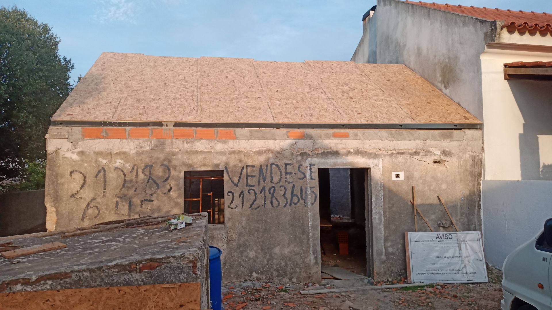 Prédio de concreto dilapidado à venda, com grafites na fachada. Telhado marrom, detalhes em tijolo aparente, portas vazias.