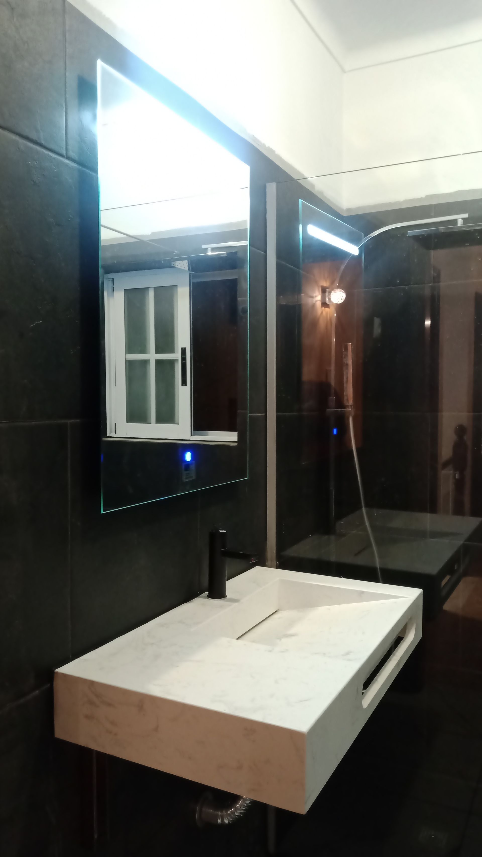 Banheiro moderno com pia branca, torneira preta e um grande espelho com iluminação LED.