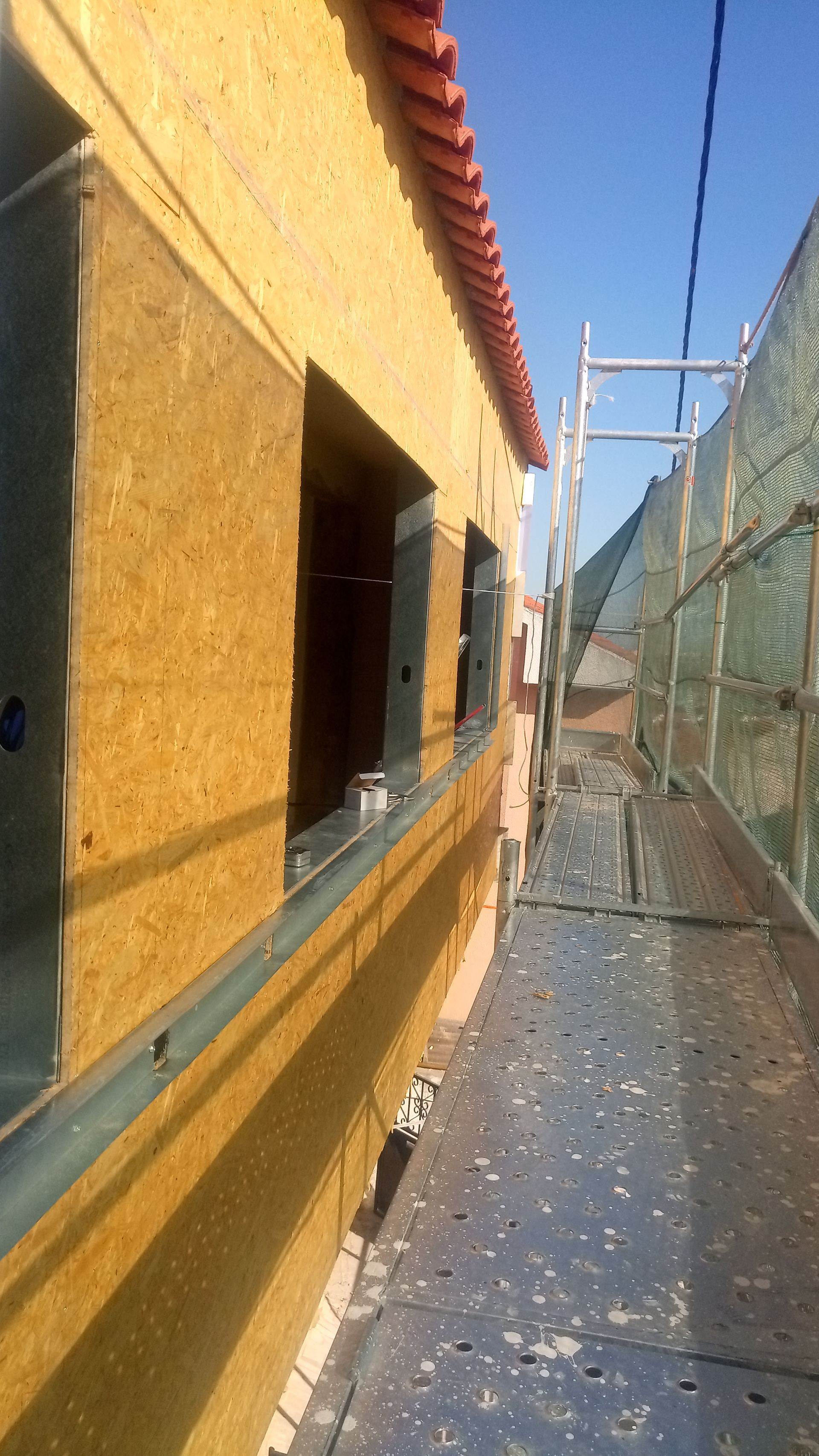 Exterior de um prédio com janelas inacabadas, andaimes de construção e um céu azul claro.