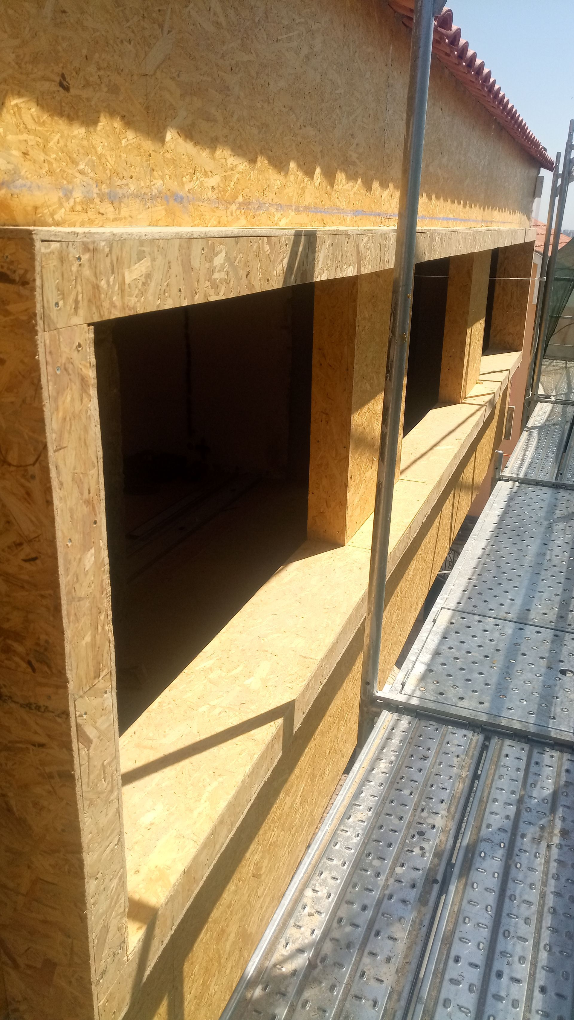 Exterior de um edifício com aberturas de janelas emolduradas em madeira, com andaimes visíveis.