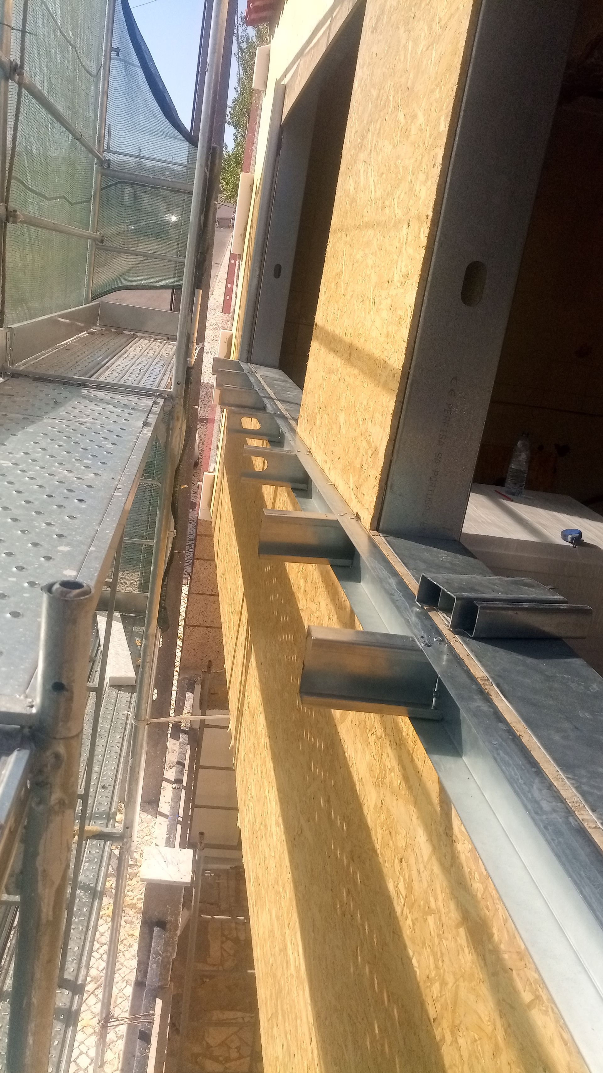 Andaimes de construção ao lado da parede de um edifício, com suportes metálicos e painéis de madeira.