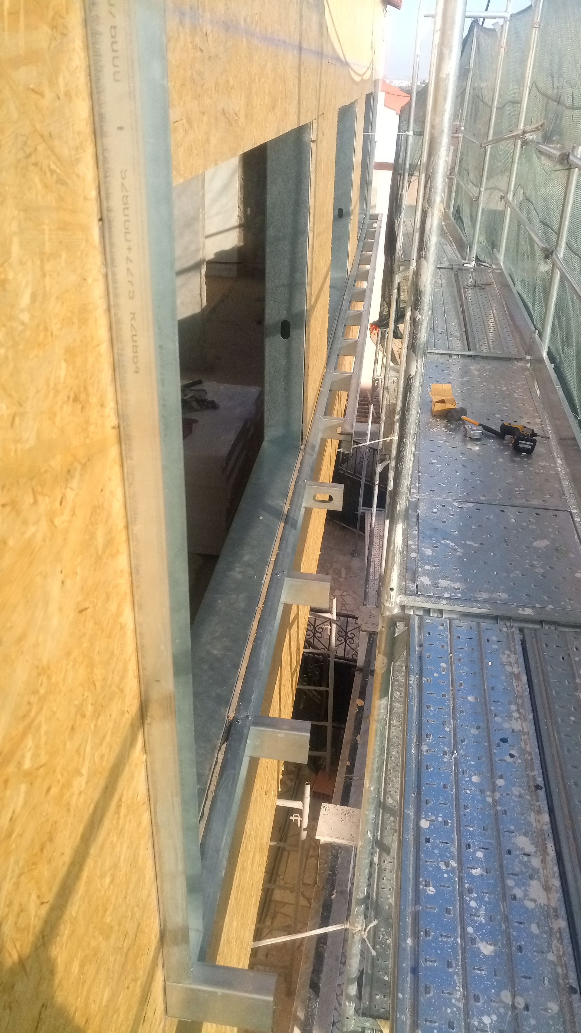 Canteiro de obras: andaimes metálicos junto à fachada de um edifício, mostrando a moldura da janela e o isolamento.
