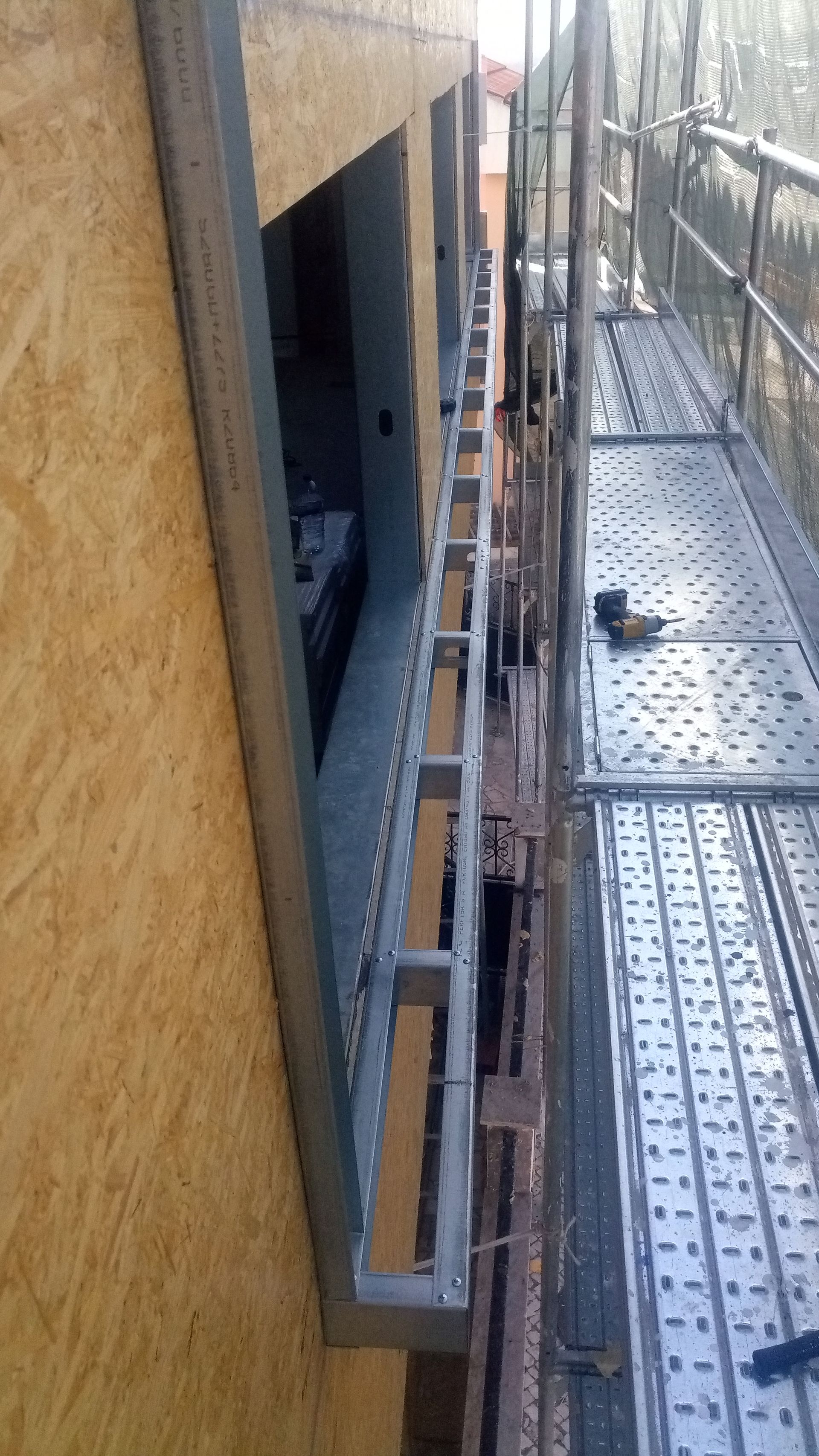 Um andaime metálico parcialmente construído ao lado da abertura externa de um edifício, com uma parede revestida de OSB.