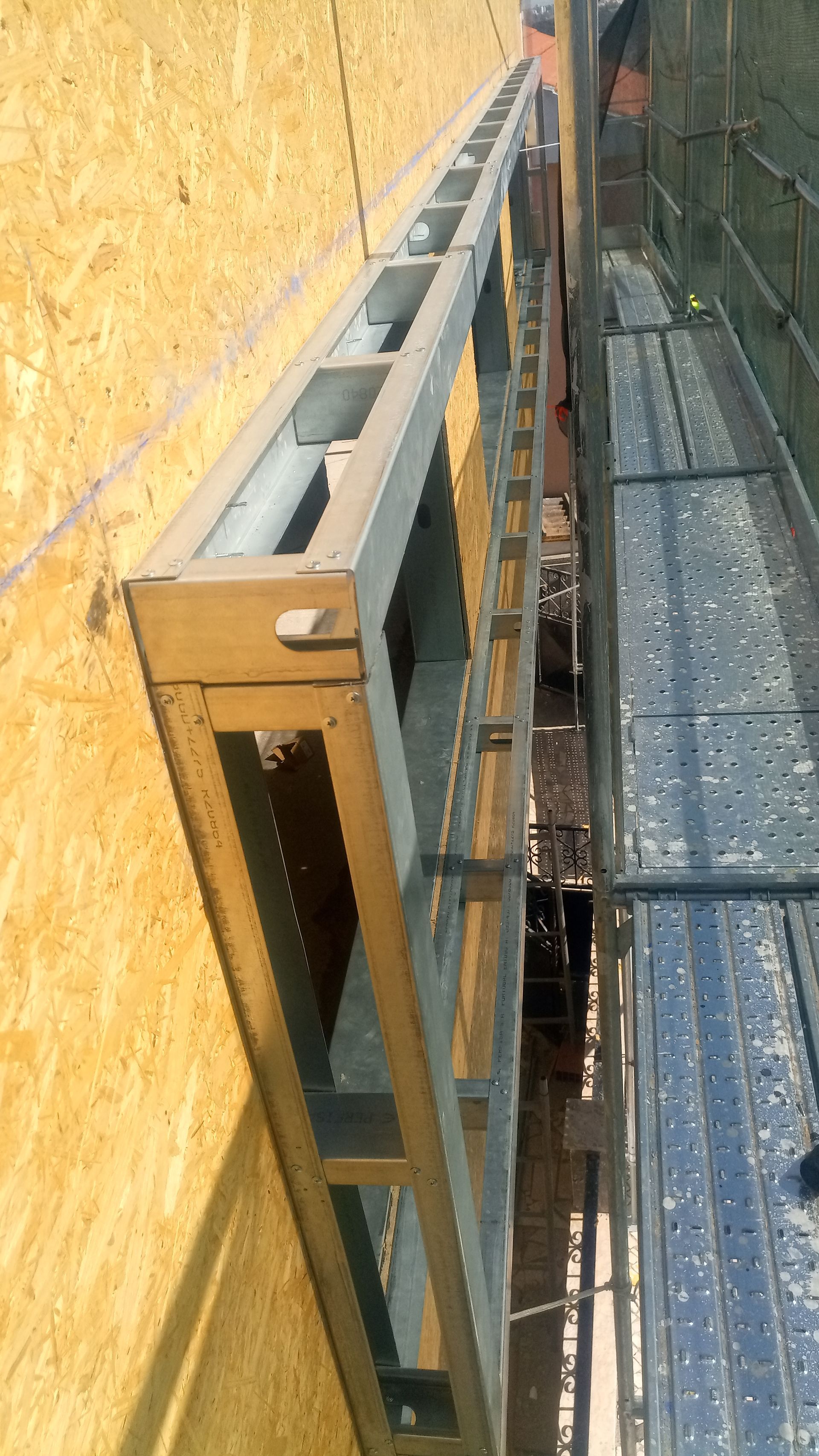Estrutura metálica instalada contra uma parede de madeira, com andaimes visíveis por baixo.