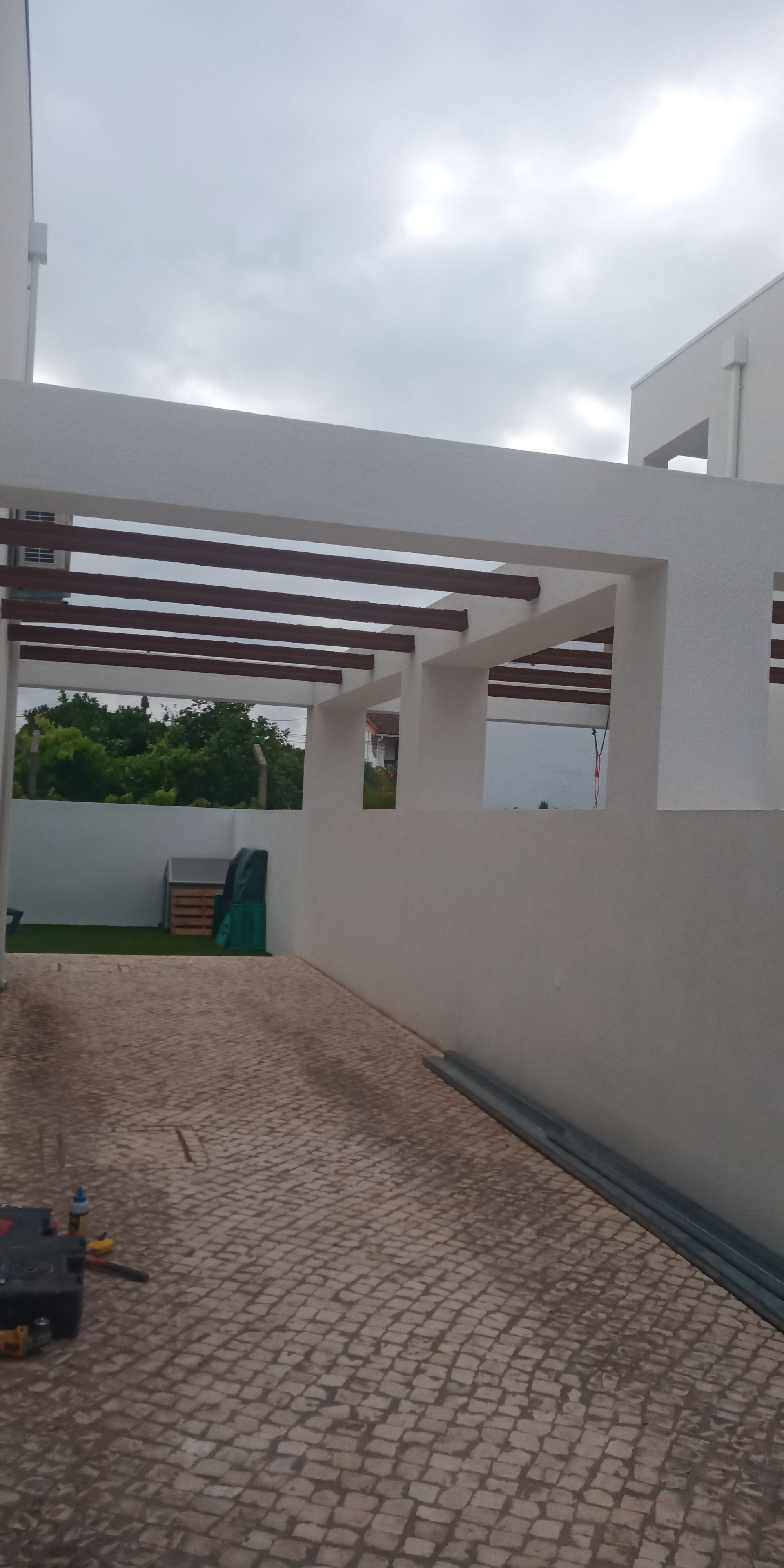 Entrada de automóveis de um prédio branco com uma pérgola, céu nublado acima.