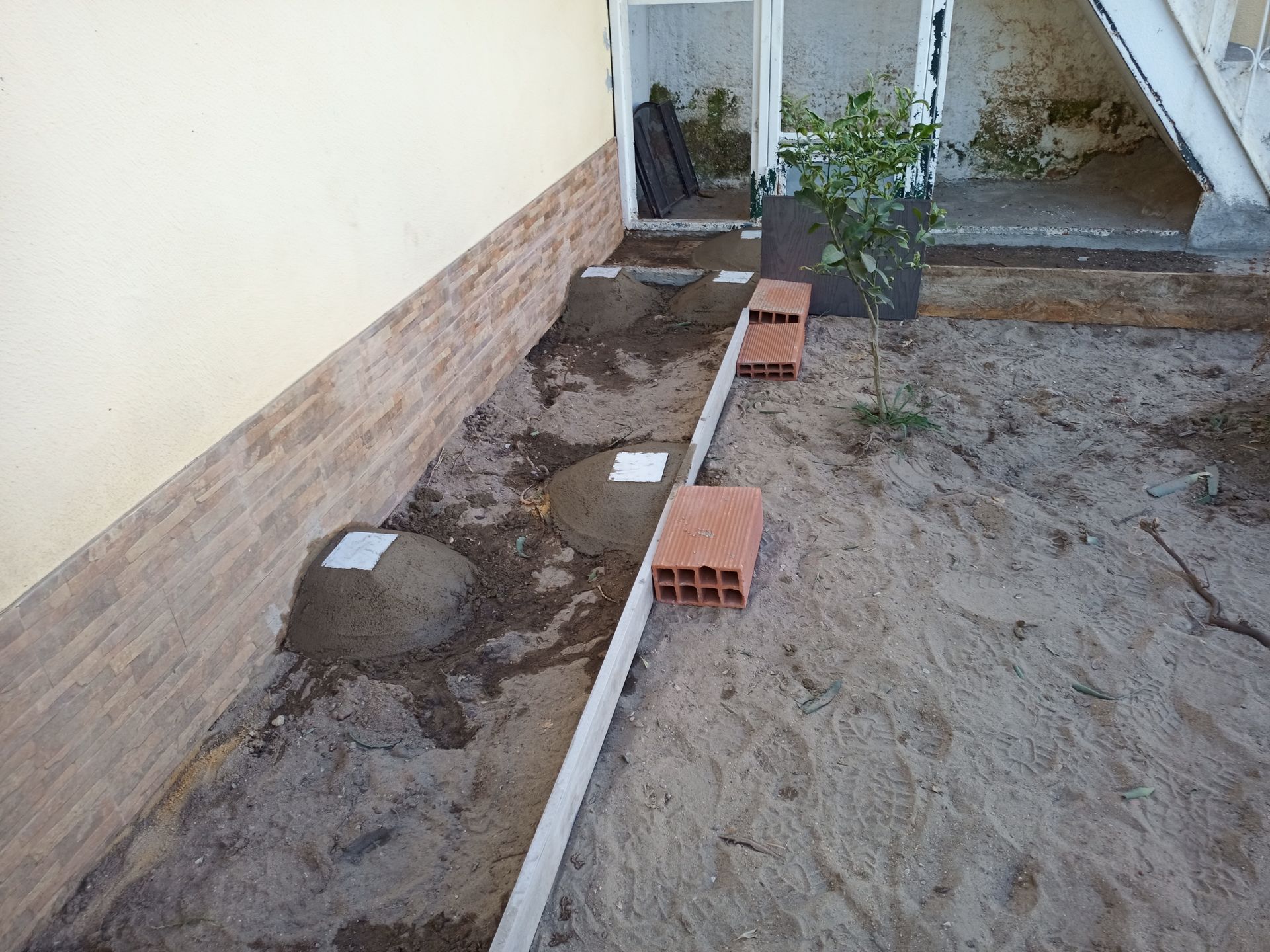 Construção de uma passarela com areia, cimento, tijolos e placas de concreto, ao lado de um edifício.