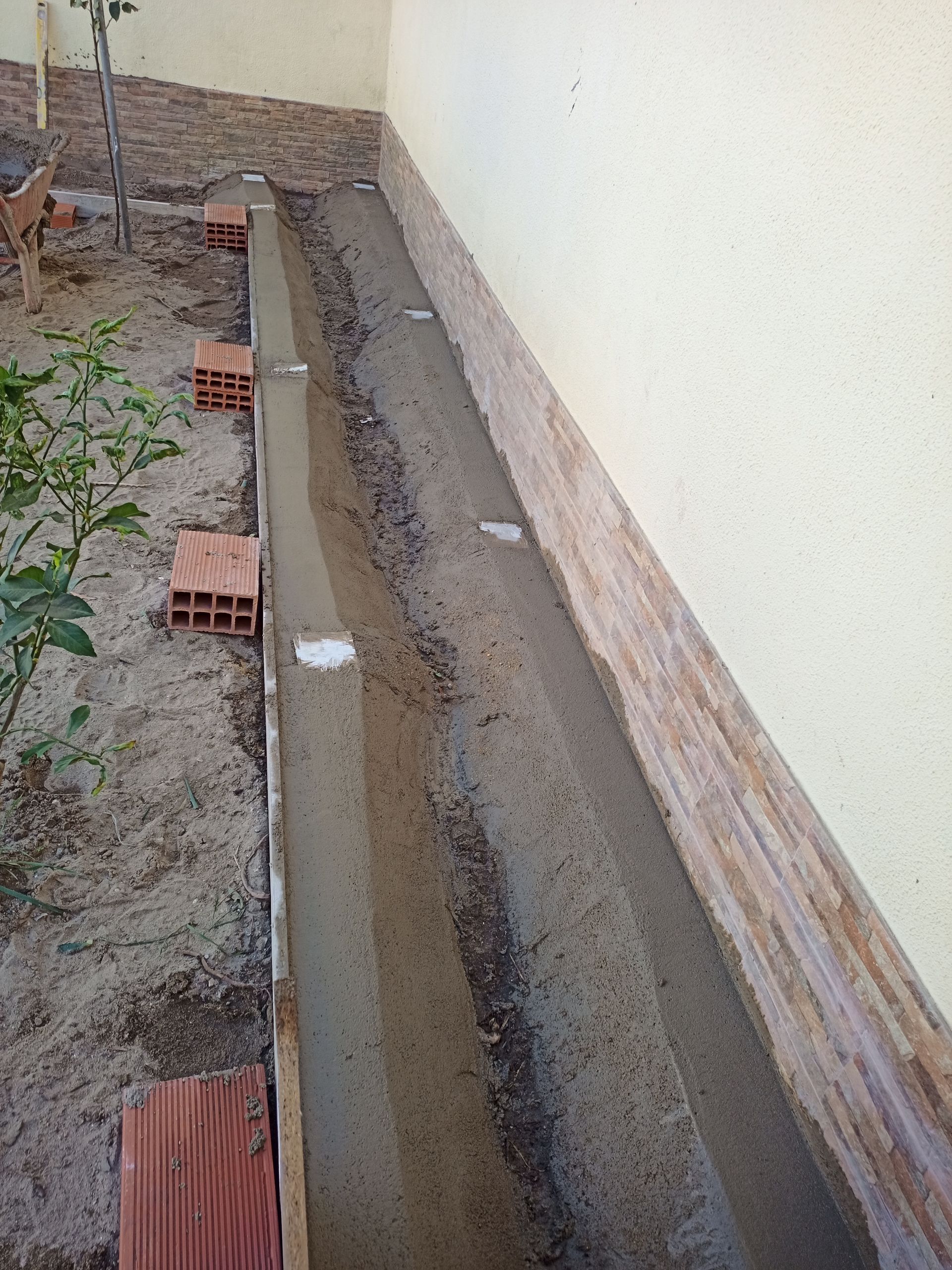 Valeta de concreto longa e estreita junto a uma parede, possivelmente para drenagem ou jardinagem.