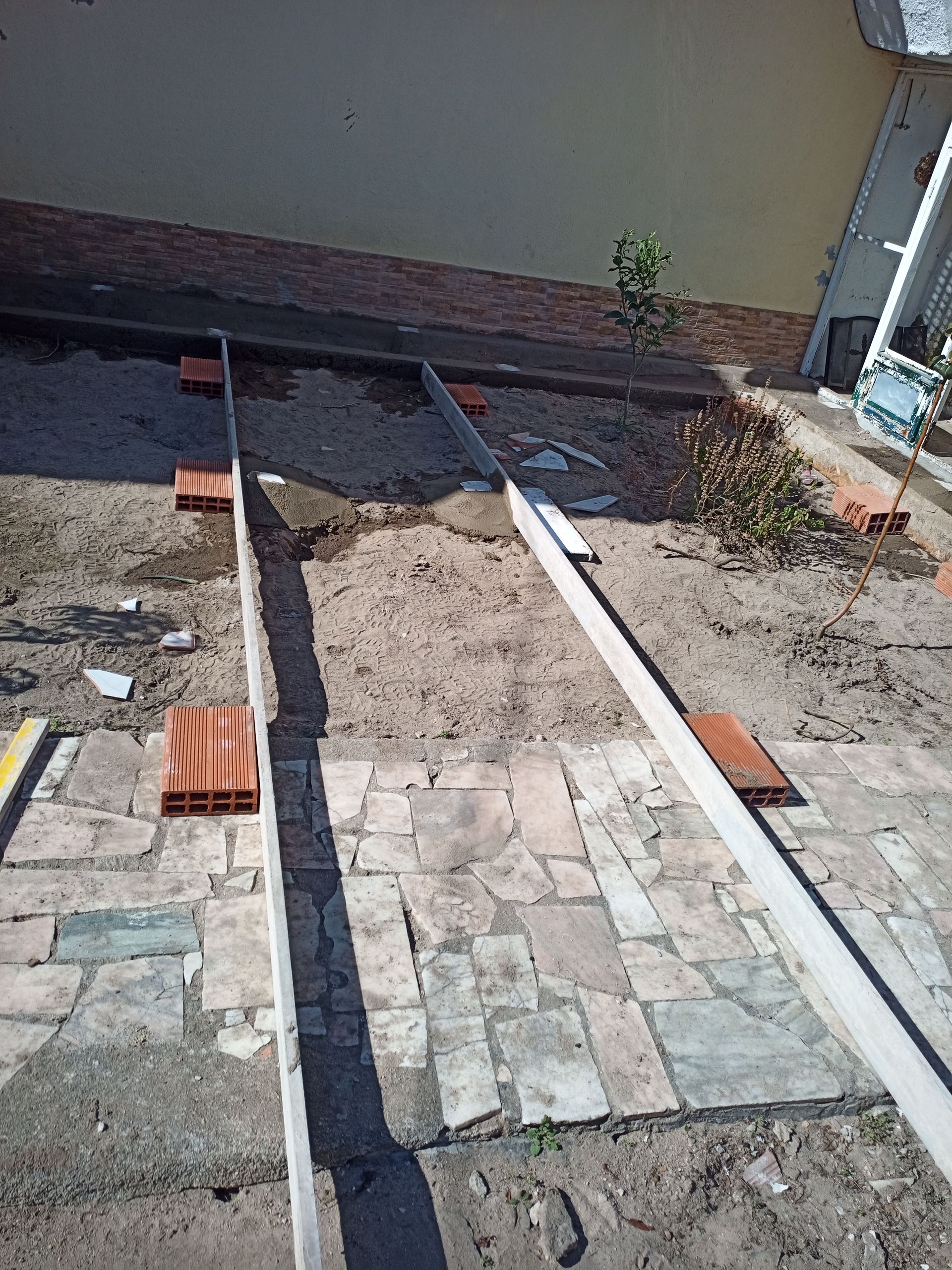 Construção da estrutura de um deck sobre um pátio de tijolos. Vigas de madeira são assentadas sobre suportes de tijolos.