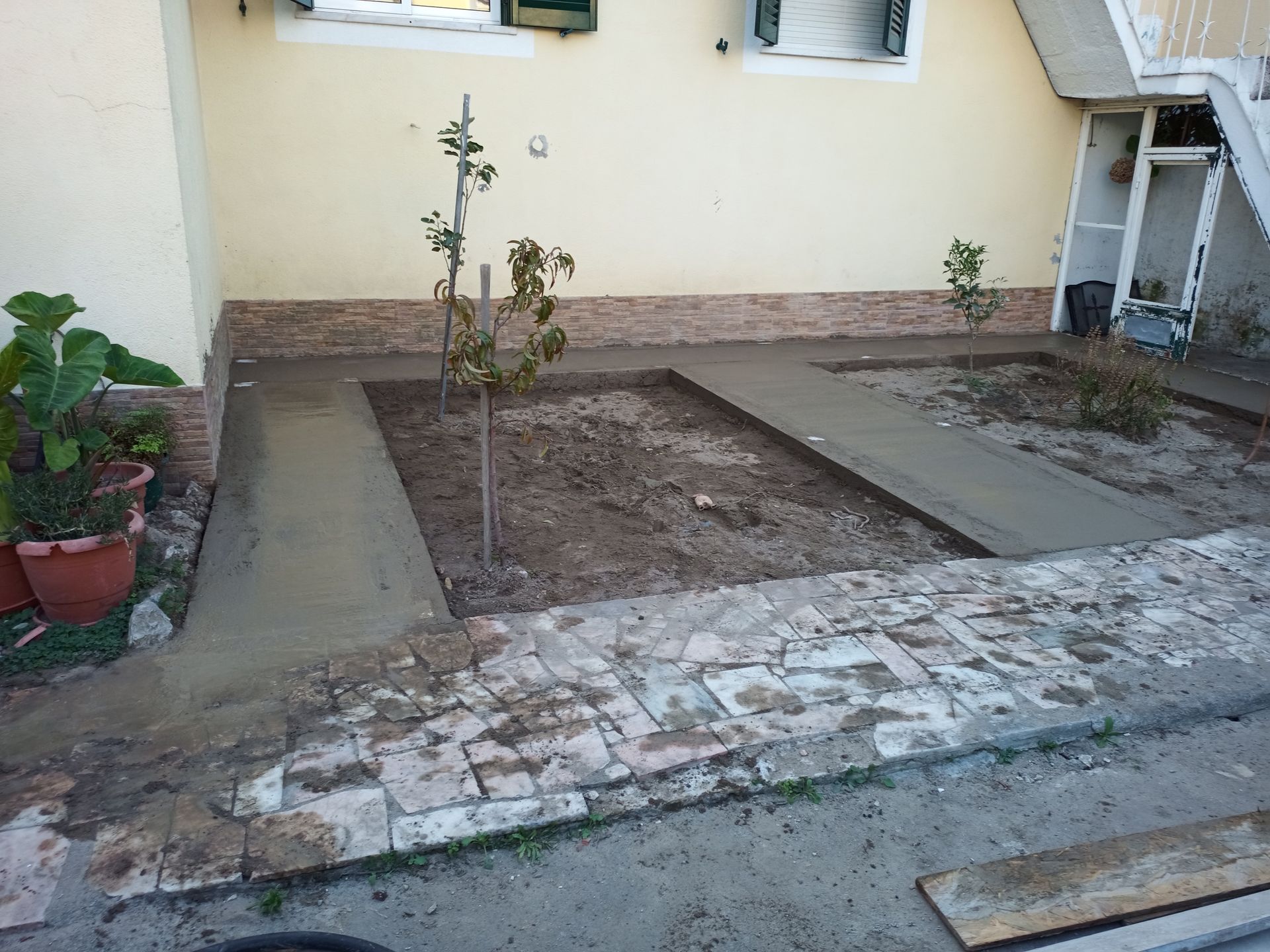 Caminhos de concreto recém-construídos em um jardim, com pequenas árvores e borda de tijolos em um ambiente residencial.