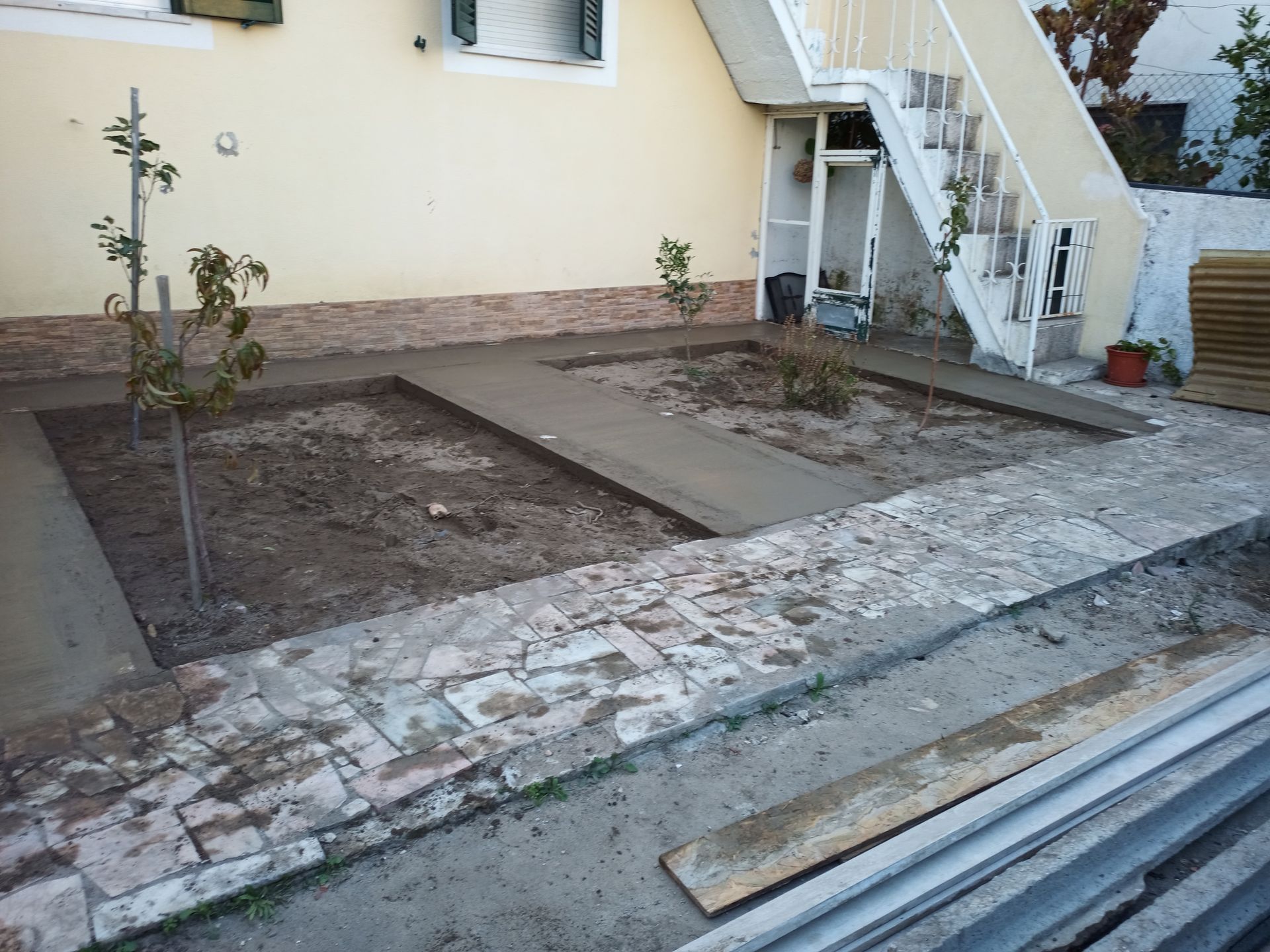 Um quintal com áreas parcialmente pavimentadas e dois canteiros retangulares.