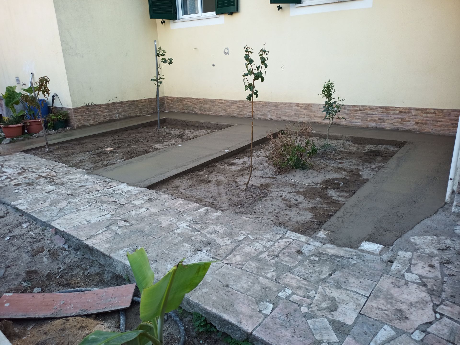 Jardim com calçadas de concreto recém-construídas e pequenas árvores.
