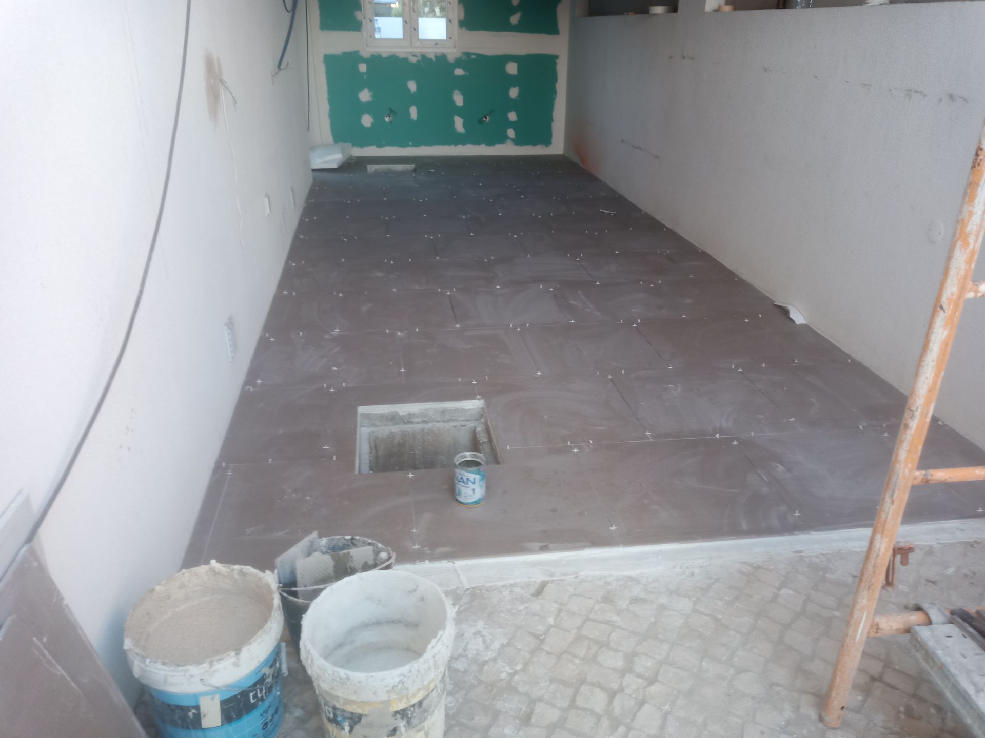 Espaço interior em construção, com piso de azulejo, paredes inacabadas e escada presente.