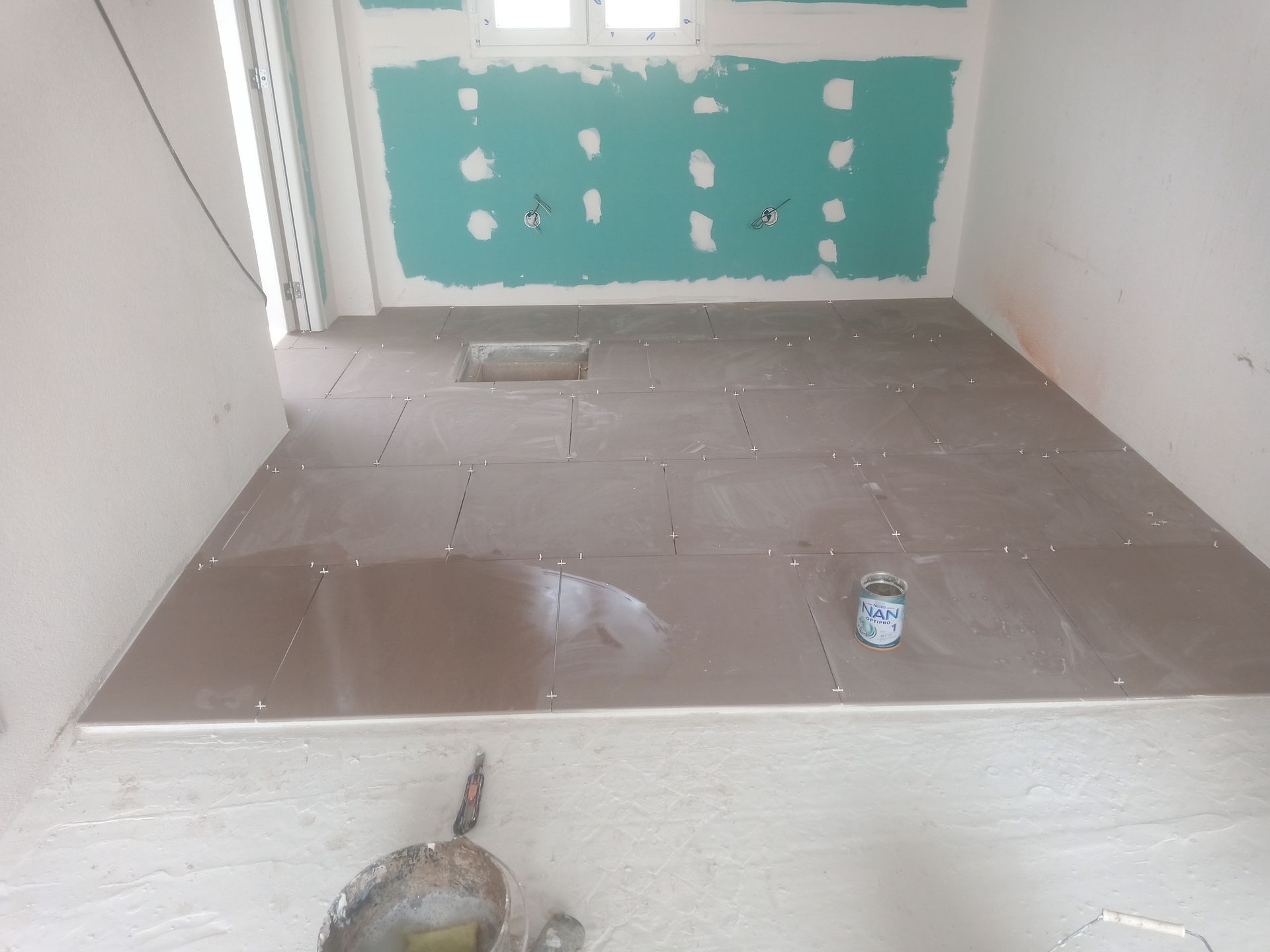 Banheiro em construção, com piso de azulejo, parede esverdeada e detalhes inacabados.