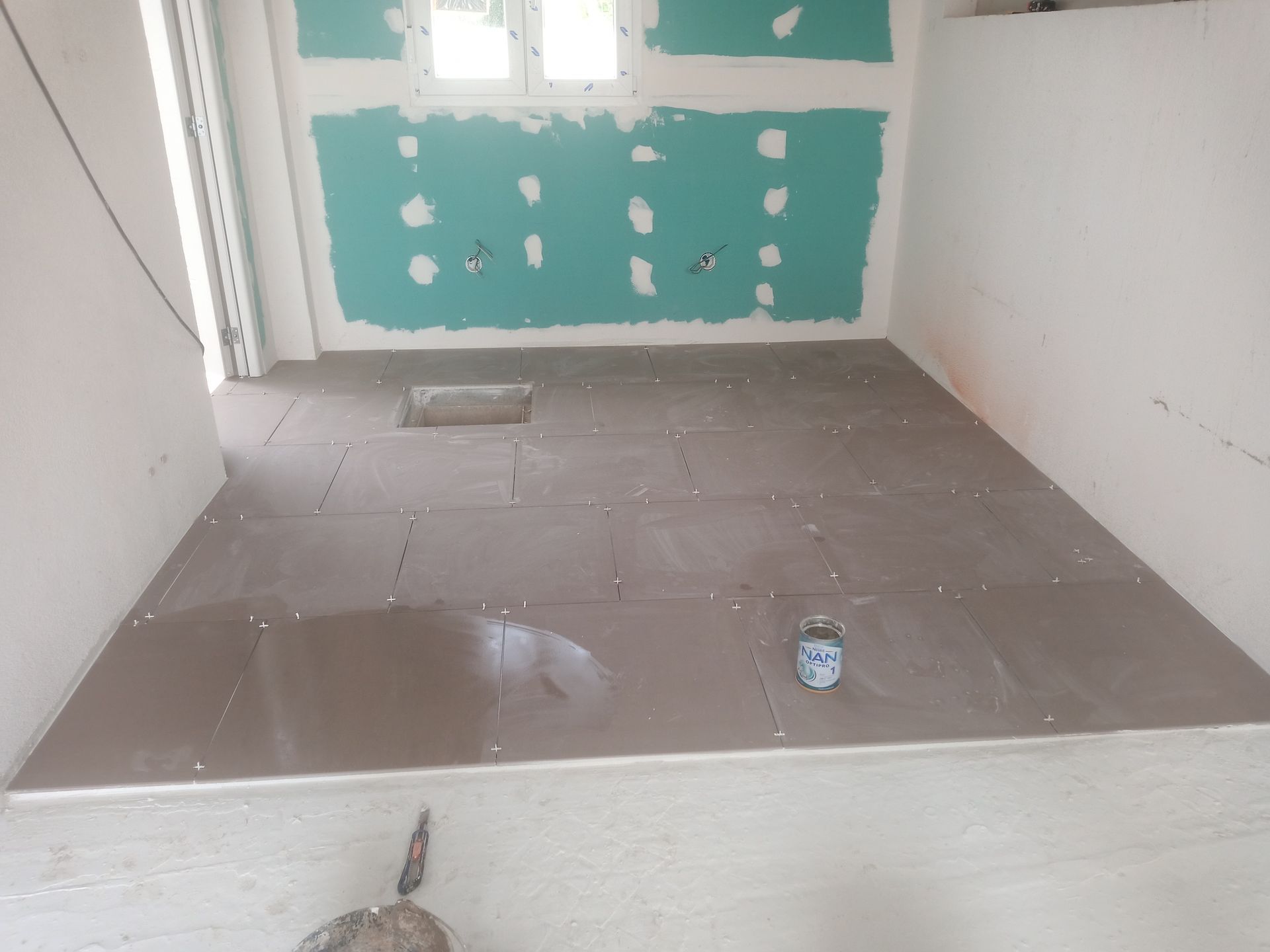 Quarto em construção com piso de ladrilho cinza, drywall verde e paredes brancas.
